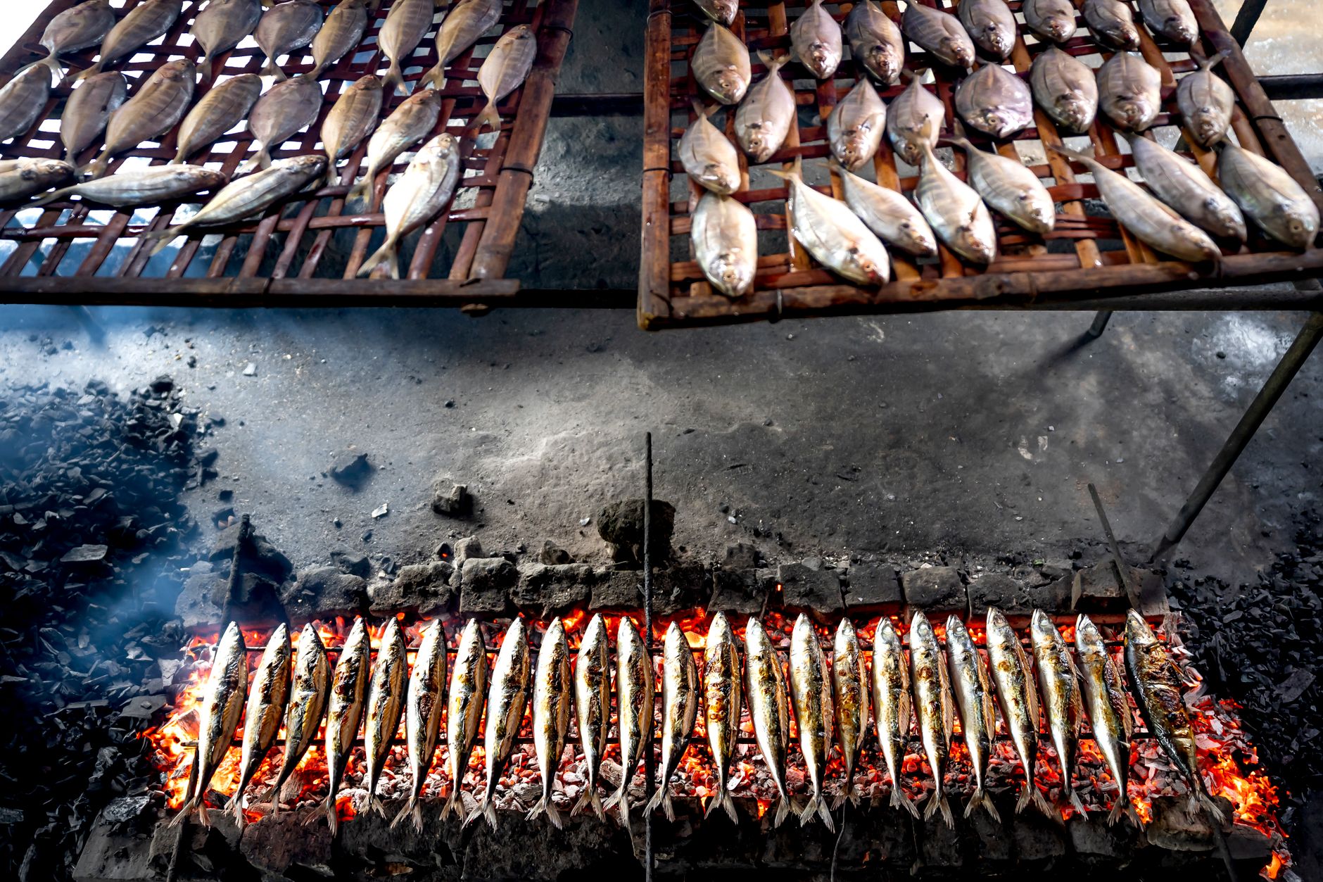 Whole fish grilling over charcoal on a bamboo rack, street-food style