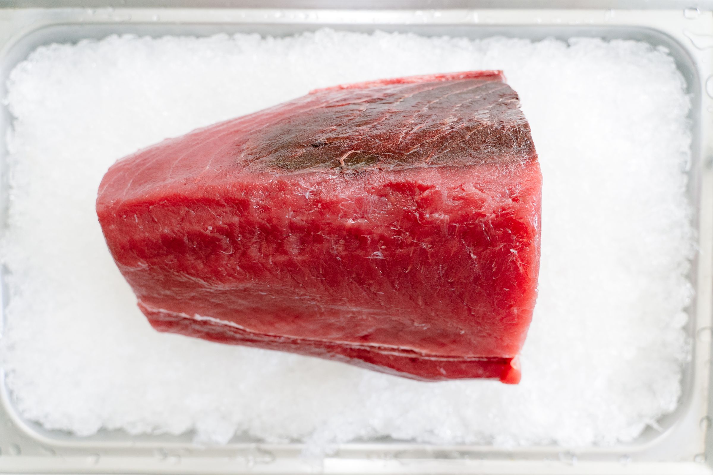 Fresh tuna loin resting on crushed ice in a steel tray
