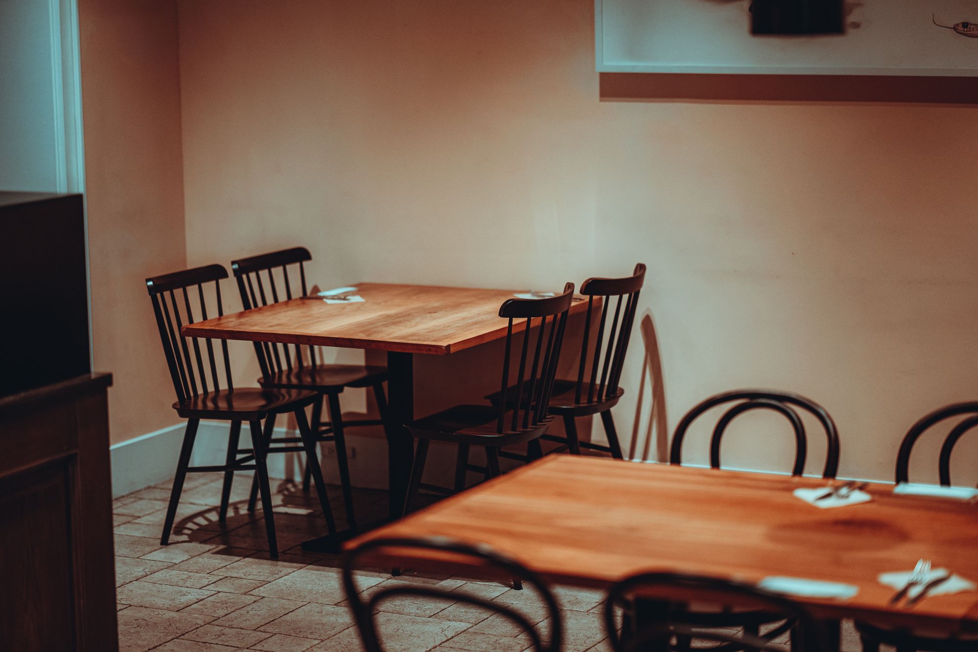 Empty wooden tables and spindle-back chairs in a warm-lit restaurant dining room