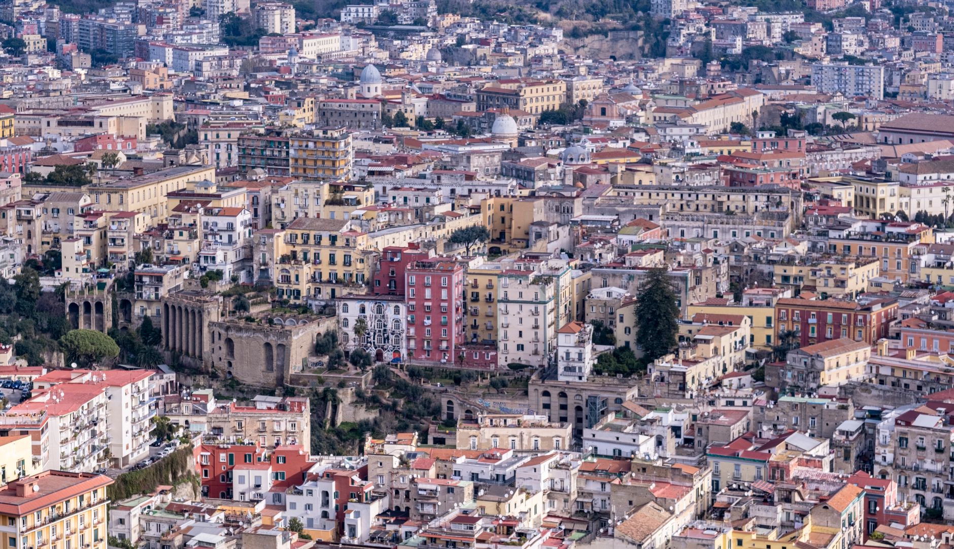 Aerial view of Naples with pastel-colored buildings and ancient ruins on a hillside