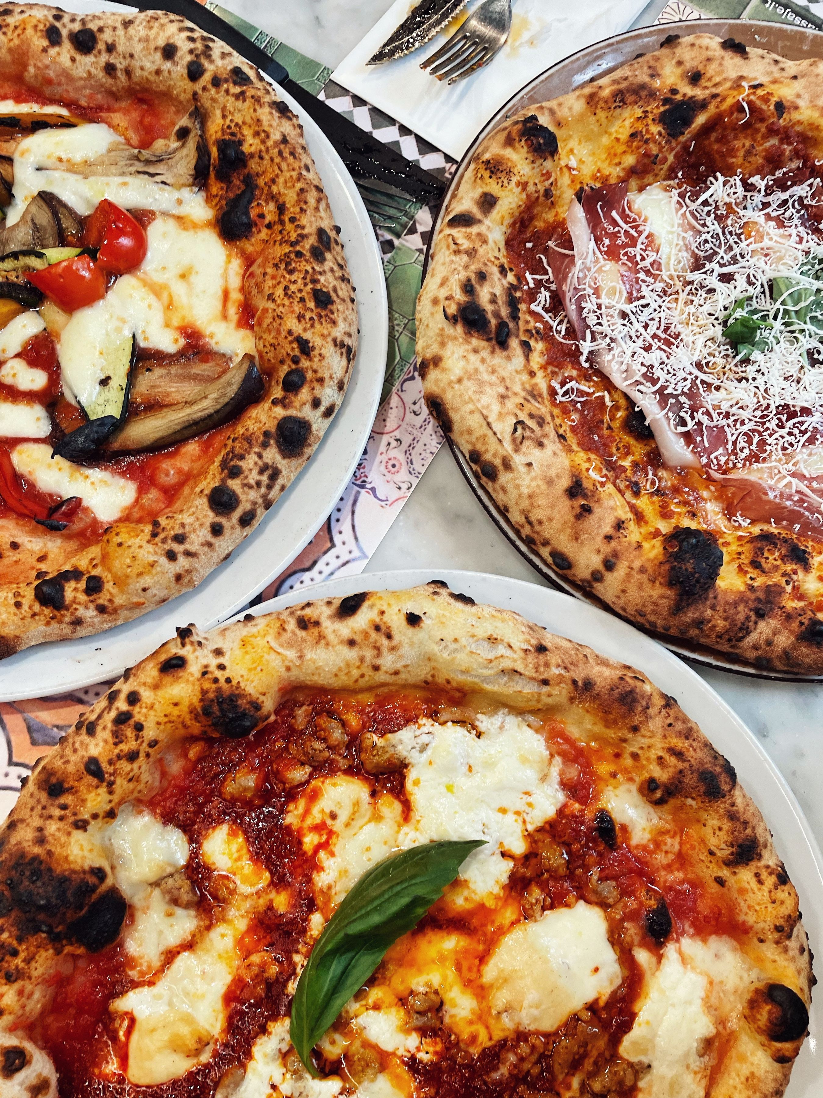 Three Neapolitan pizzas with charred, blistered crusts on a marble restaurant table