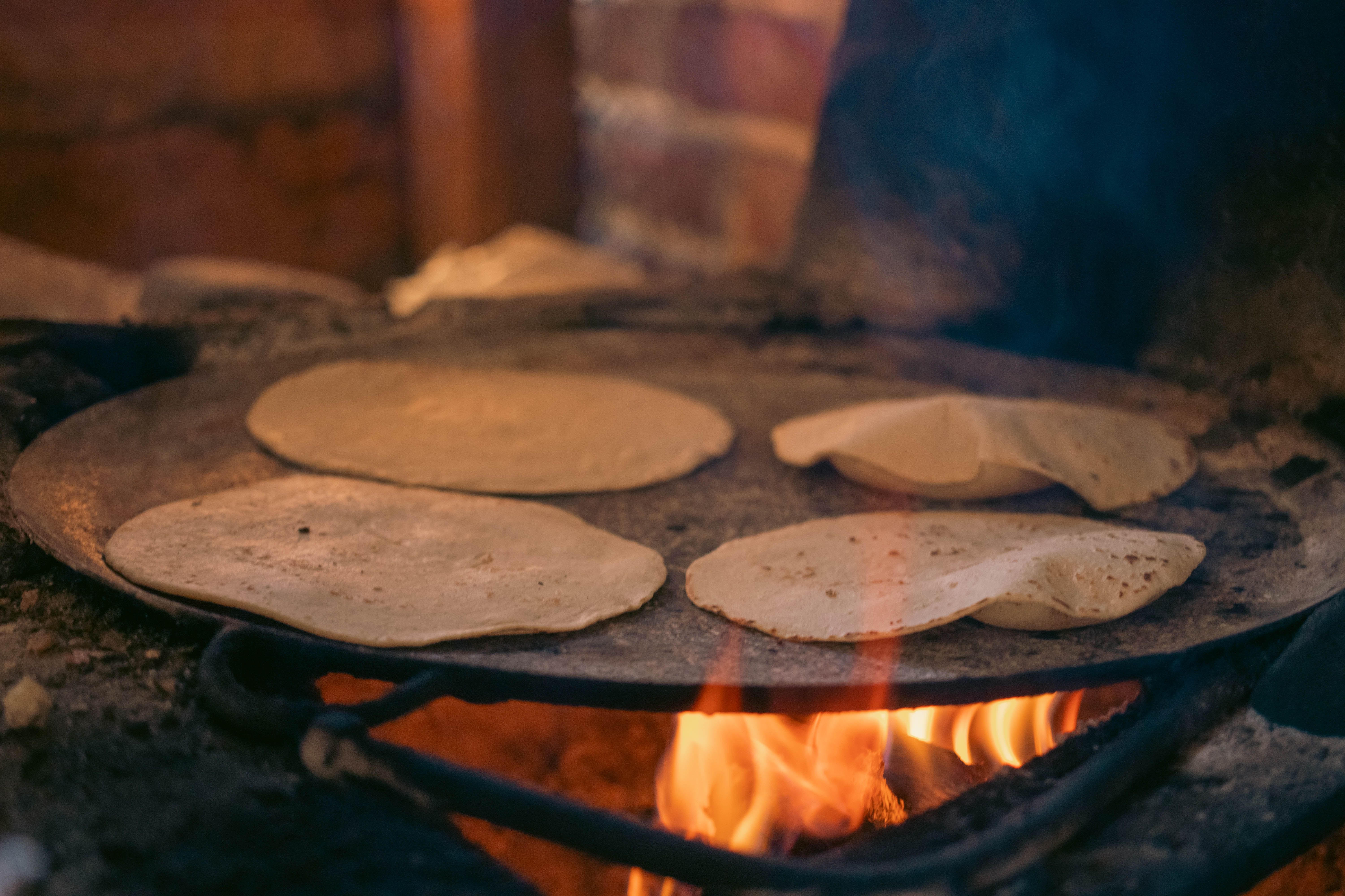 Fresh corn tortillas cooking on a wood-fired comal over open flame