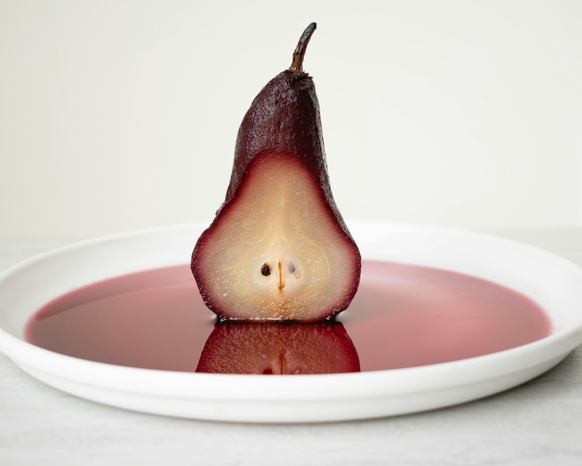 Half a pear poached in red wine standing in a pool of dark syrup on a white plate