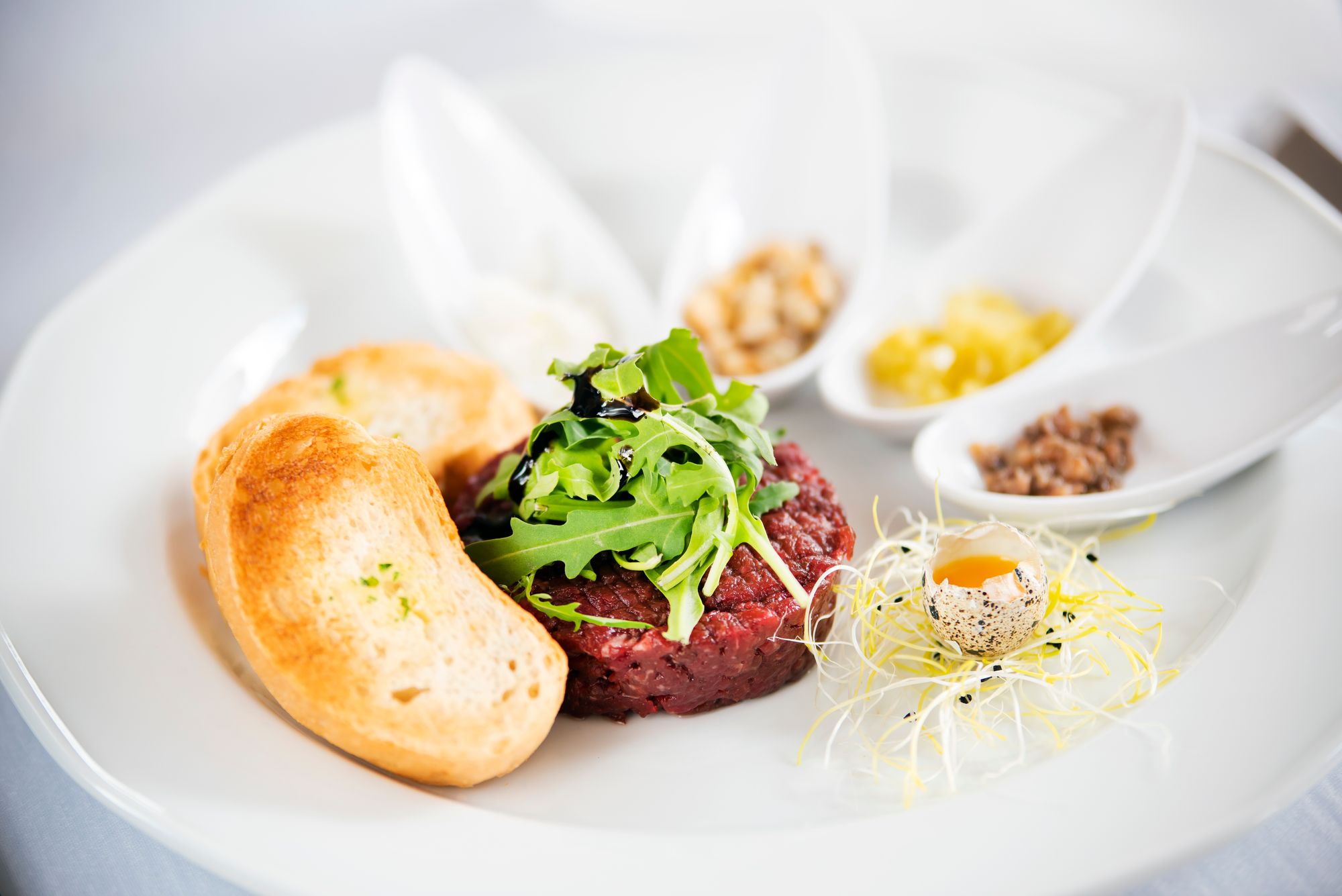 Steak tartare with toasted bread, rocket and a quail egg yolk on a white plate