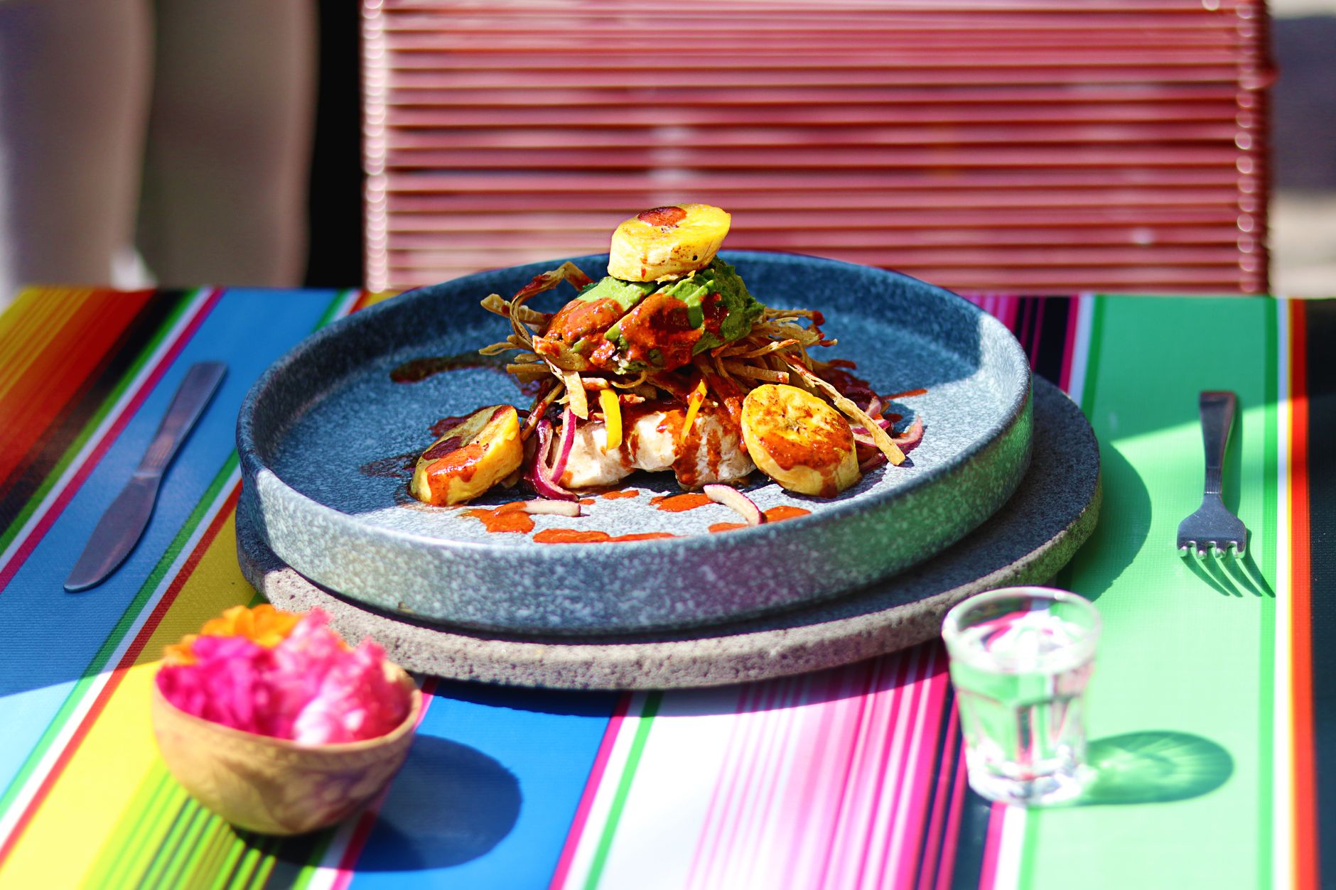 Buntes mexikanisches Gericht mit gegrillter Beilage auf einer gestreiften Tischdecke