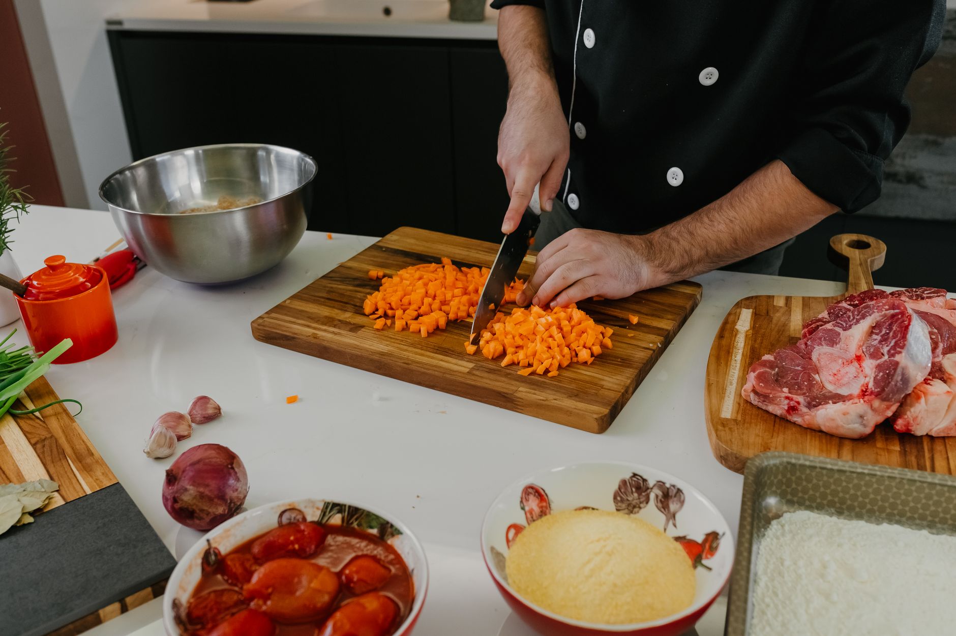 Ein Koch schneidet Karotten auf einem Holzbrett neben rohem Fleisch und Tomaten