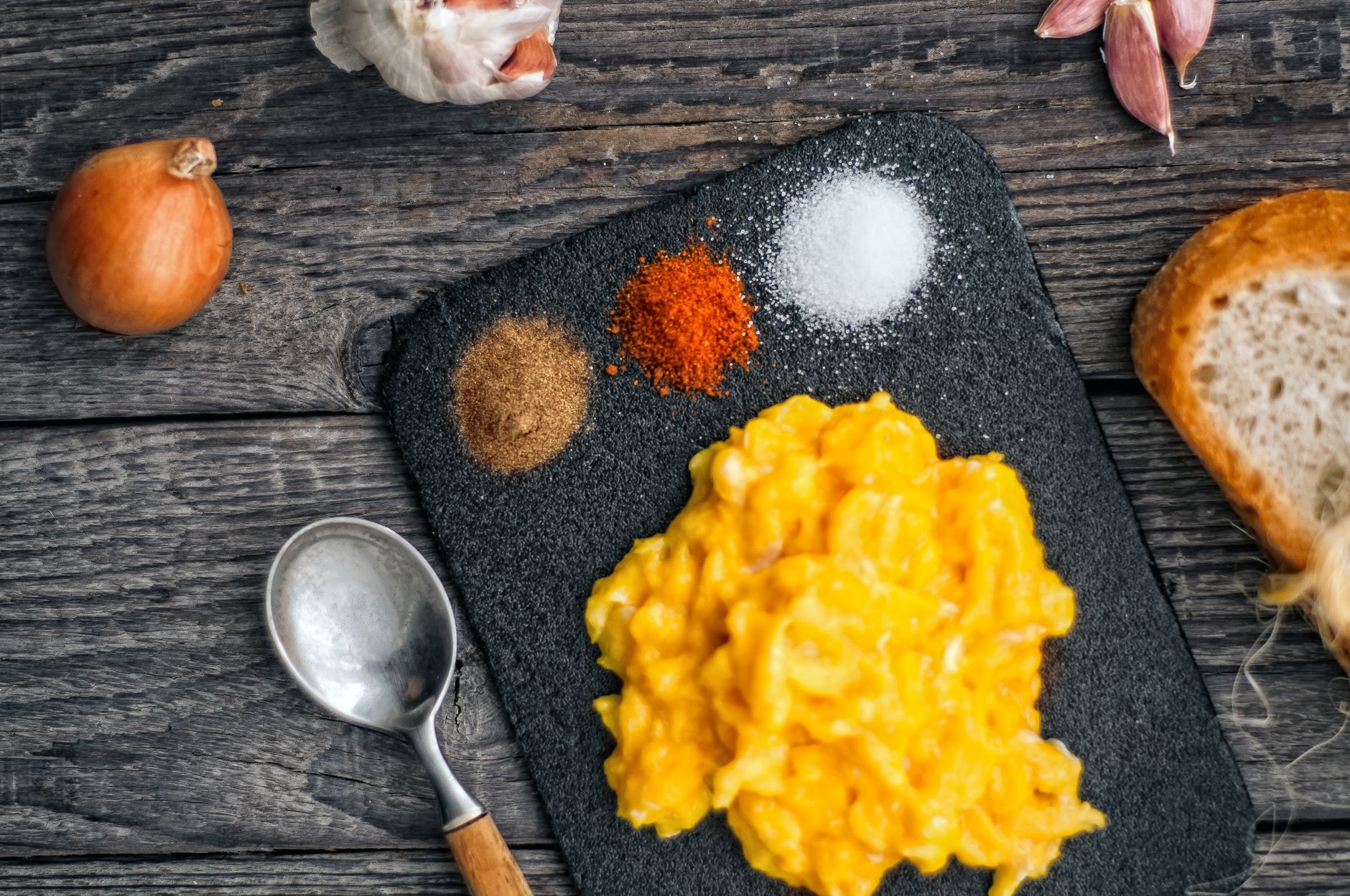 Creamy soft-scrambled eggs mounded on a dark plate, glossy and freshly cooked