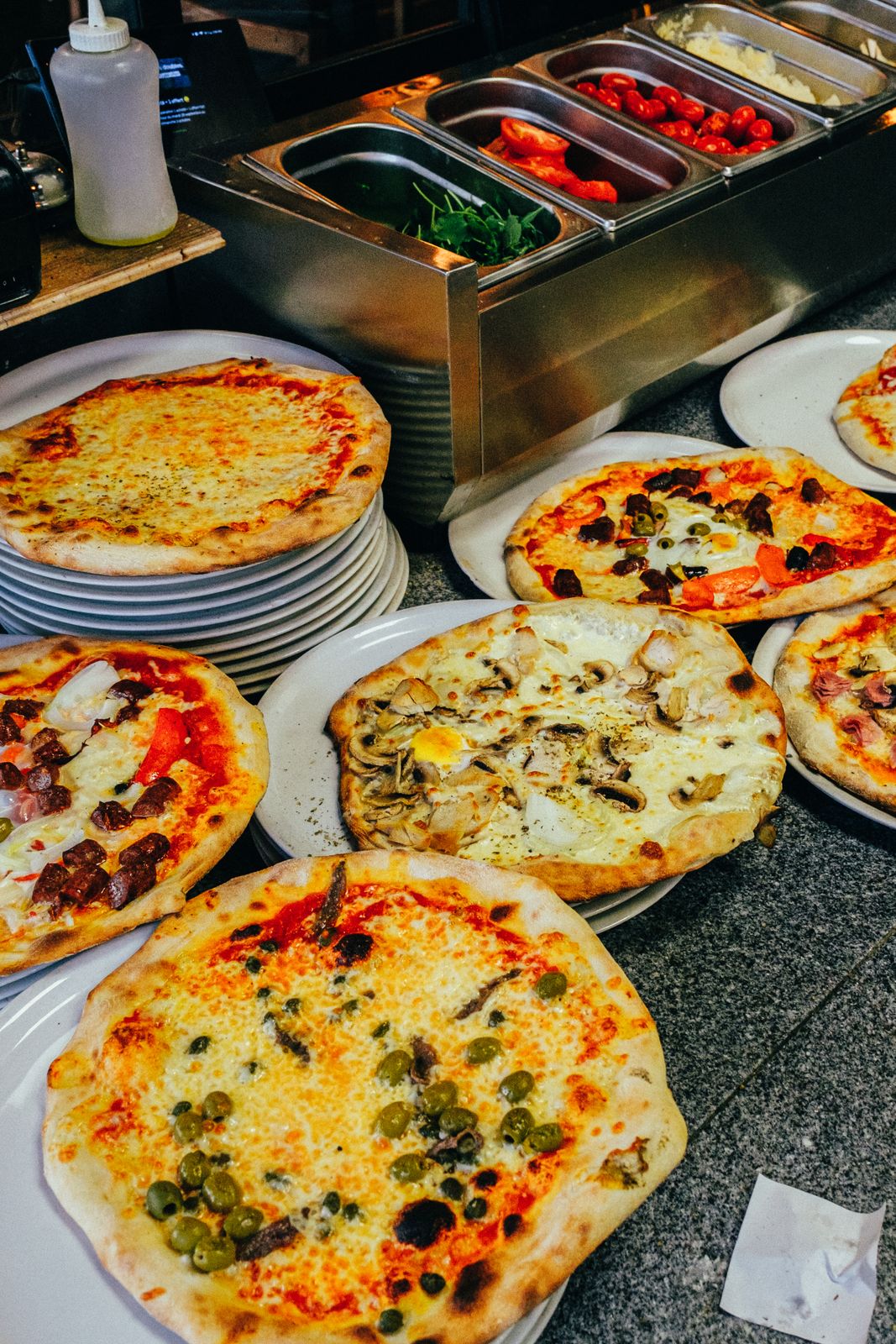 Plusieurs pizzas fraîchement cuites aux garnitures variées, présentées sur des assiettes blanches au comptoir