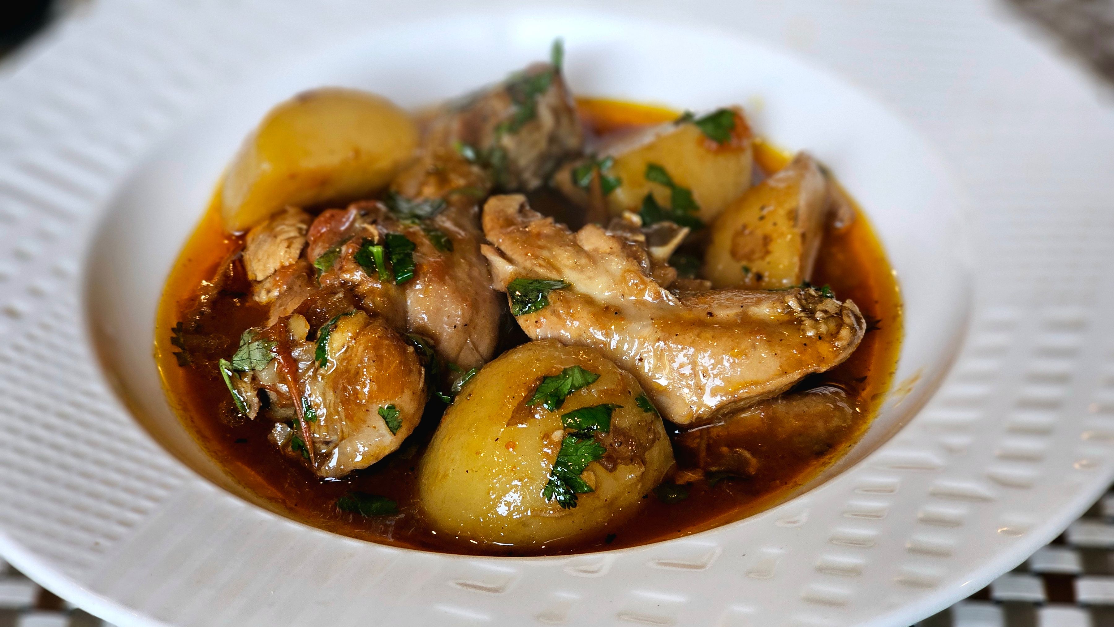 A rustic bowl of braised chicken pieces and potatoes in a rich wine sauce with parsley