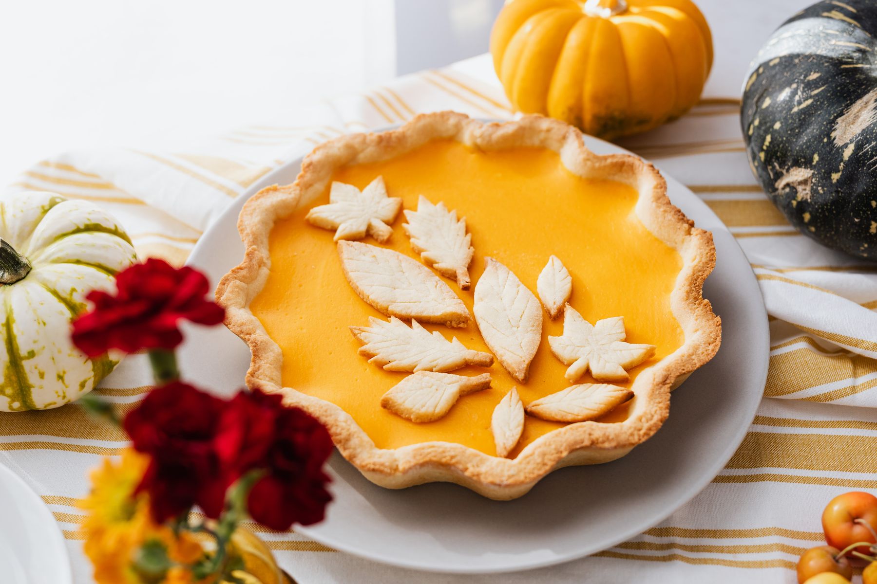 A baked pumpkin pie topped with pastry leaf cut-outs next to whole pumpkins