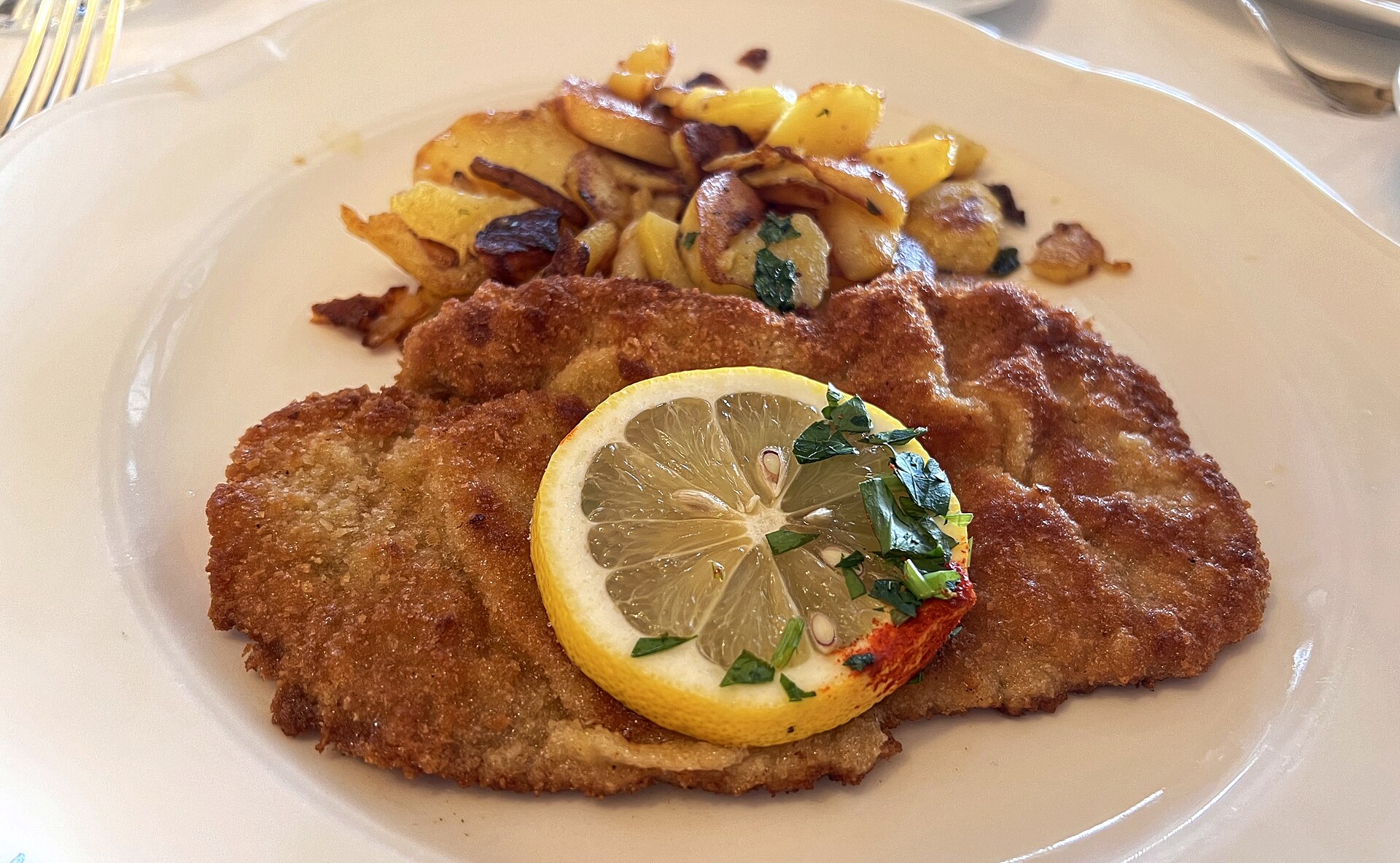 Paniertes Schnitzel mit Zitronenscheibe und Bratkartoffeln auf einem weißen Teller im Restaurant