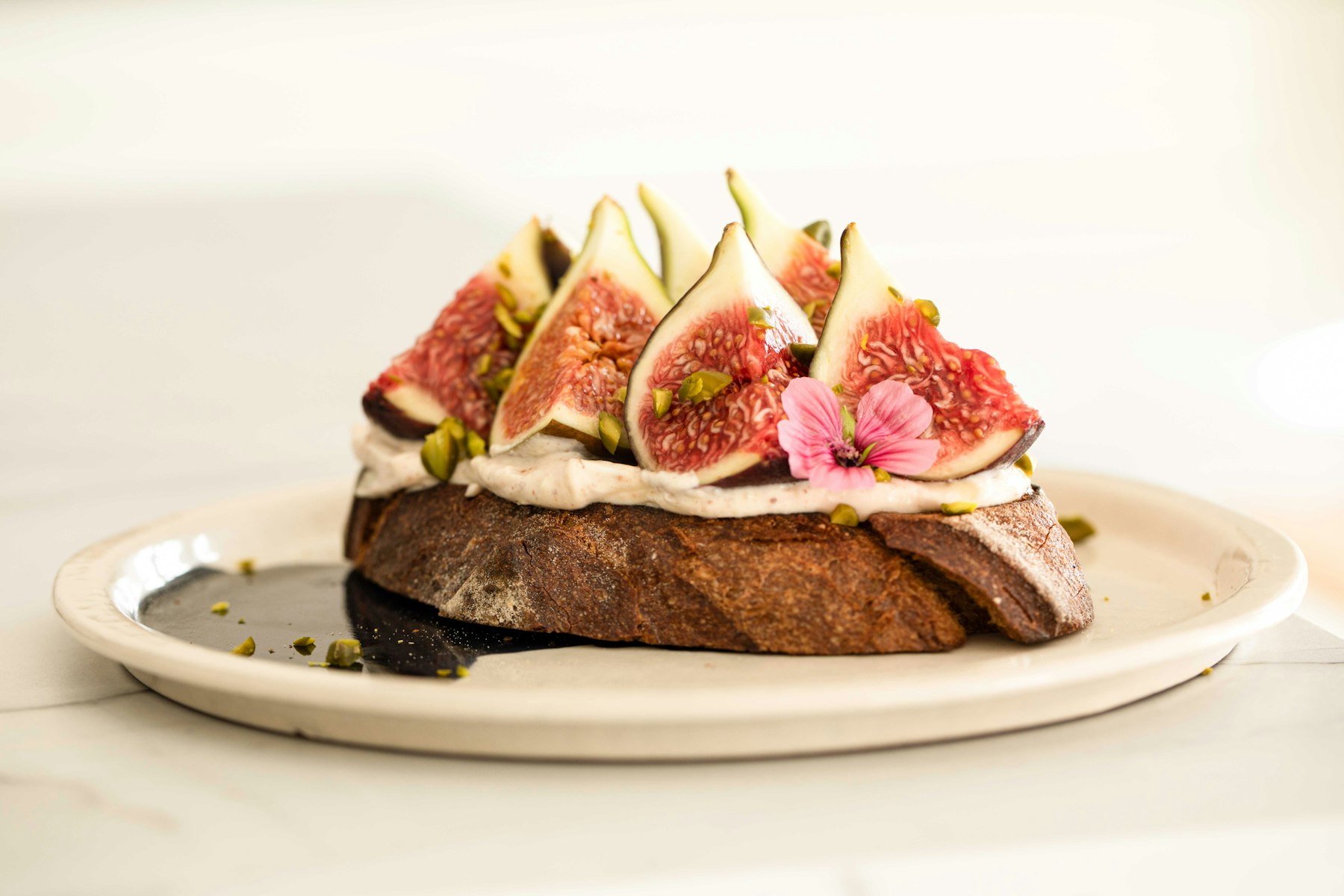 Ripe figs sliced open over creamy cheese on toasted bread with crushed pistachio