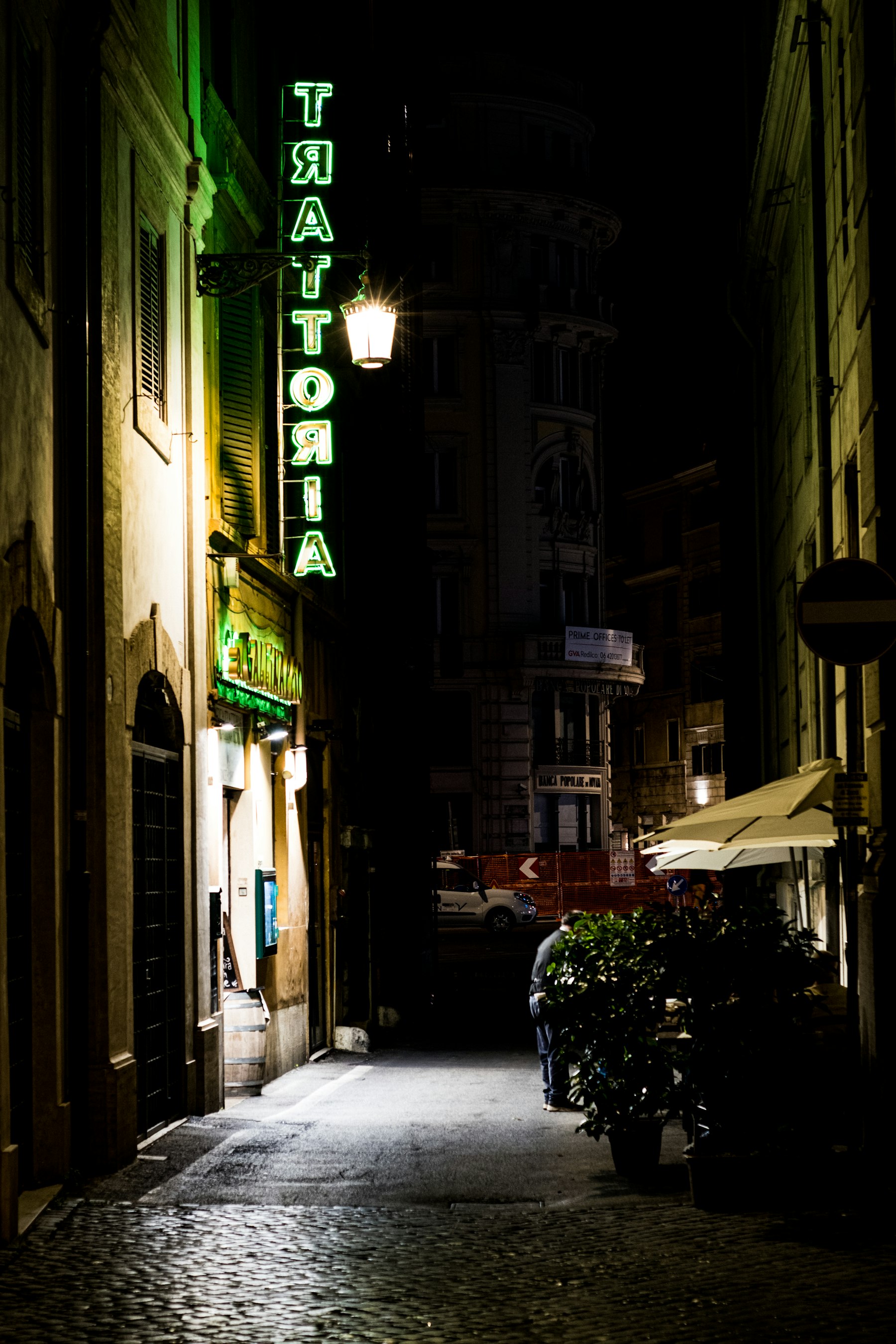 A lit trattoria sign glowing above a narrow Rome alley at night