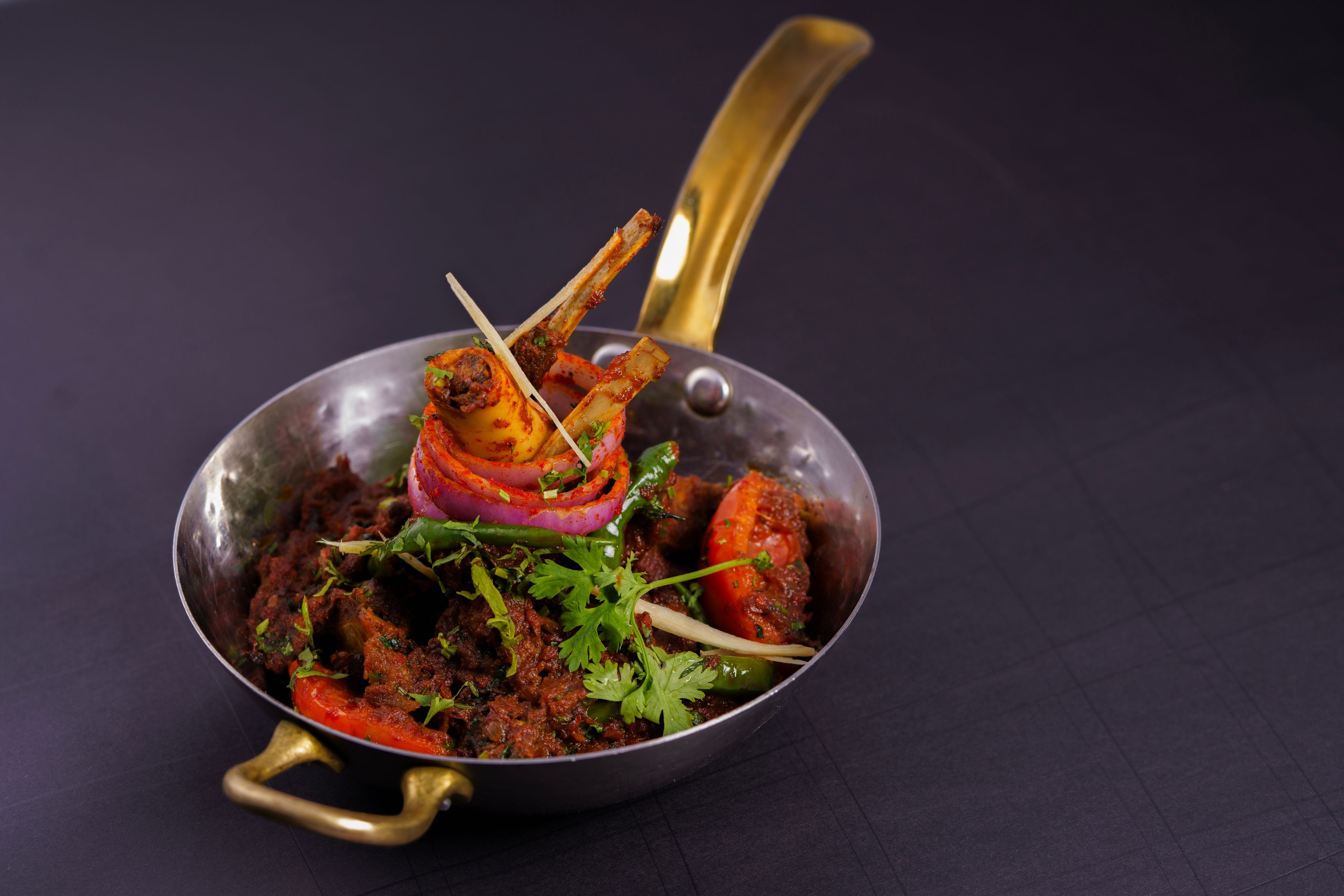 Spiced lamb chops and vegetables served in a metal kadai on a dark table
