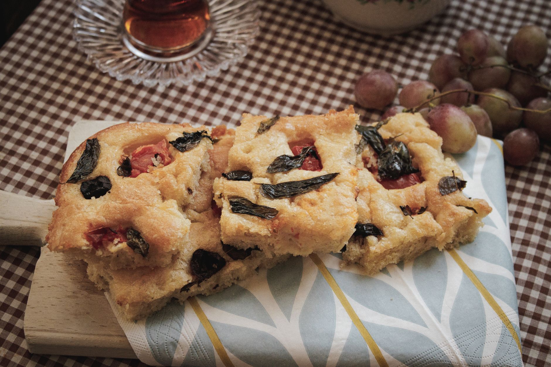 Golden baked schiacciata all'uva flatbread studded with whole dark grapes on a wooden board