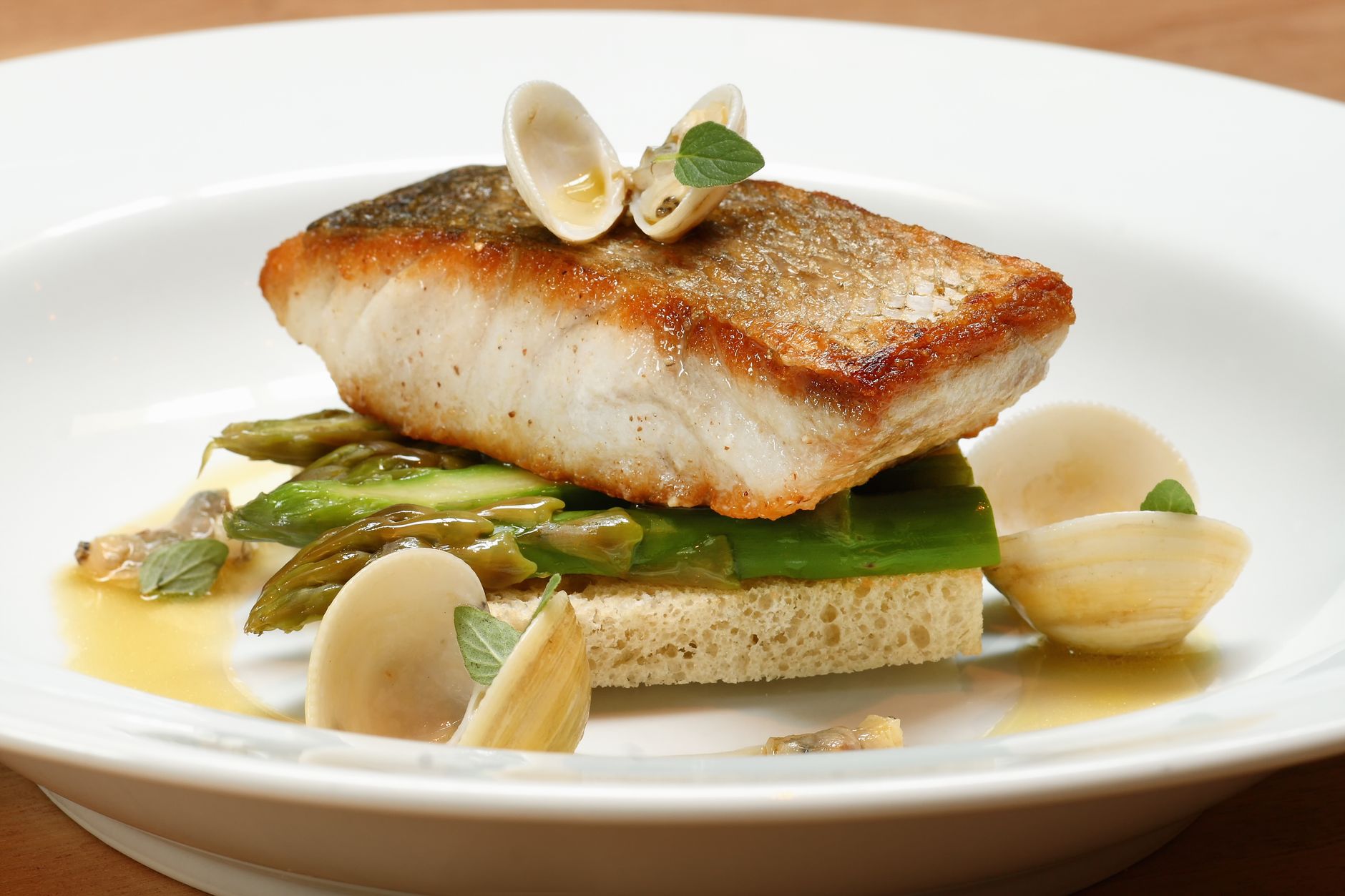 Seared fish fillet with clams and asparagus on a white fine-dining plate