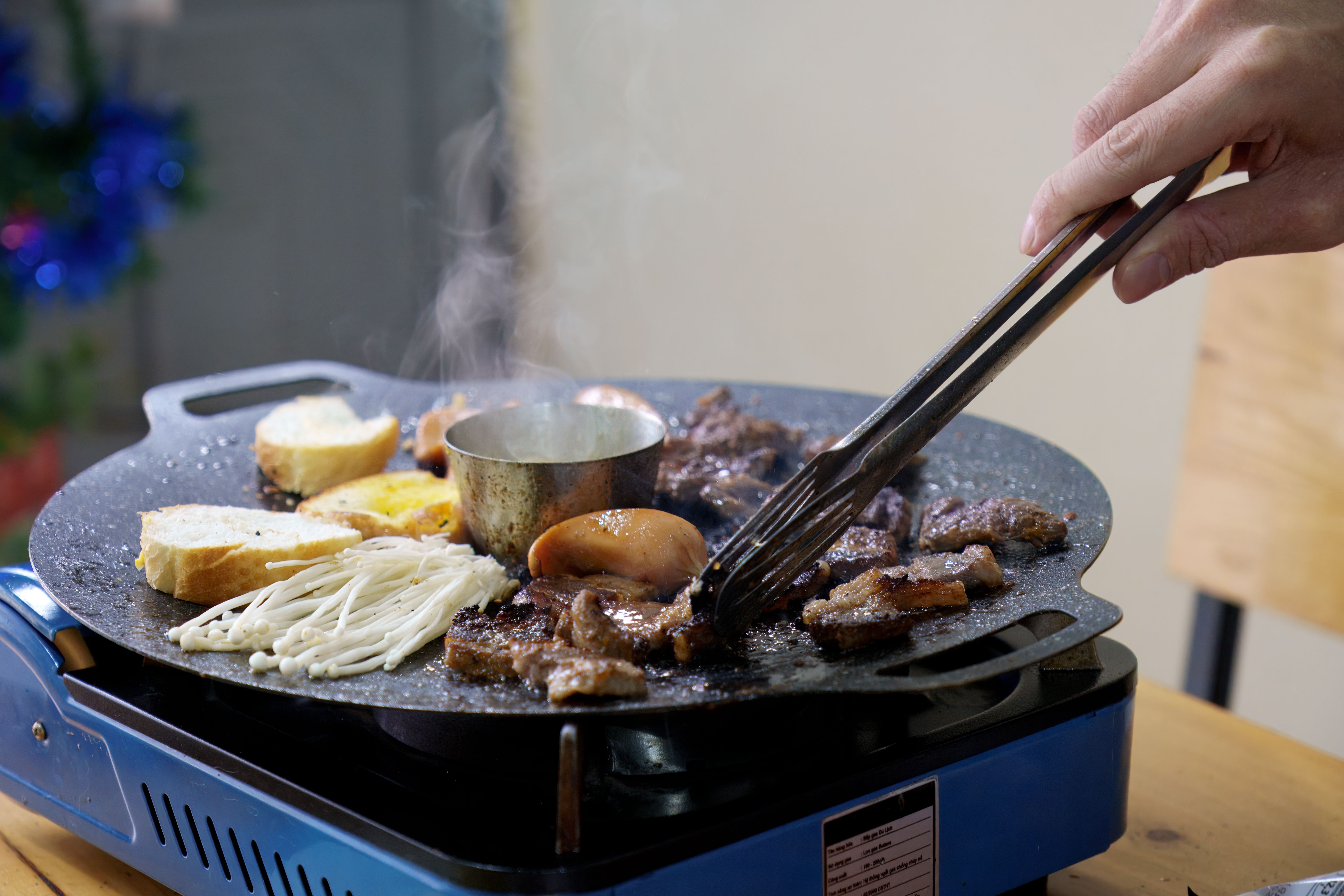Meat and enoki mushrooms searing on a tabletop grill plate