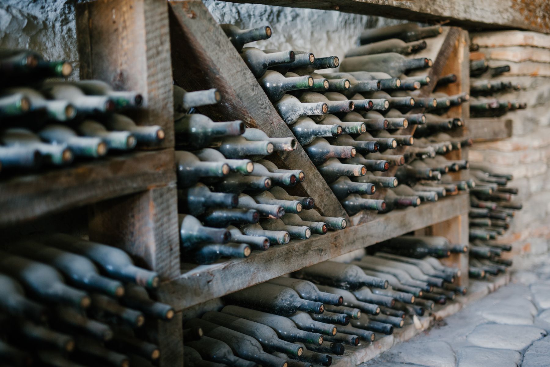 Rows of dusty aged wine bottles racked in a stone cellar