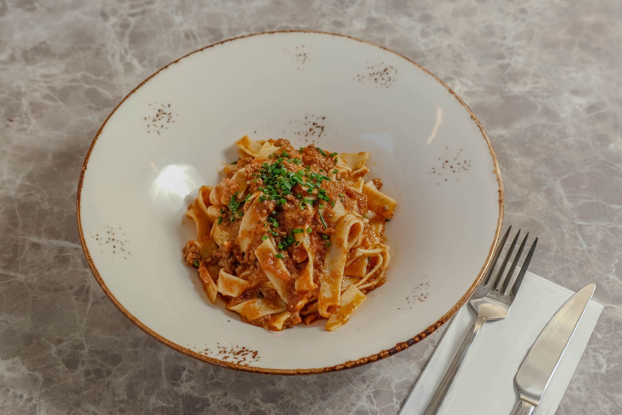 Frische Eiertagliatelle mit Fleischragù und Schnittlauch in einer weißen Schale auf Marmor