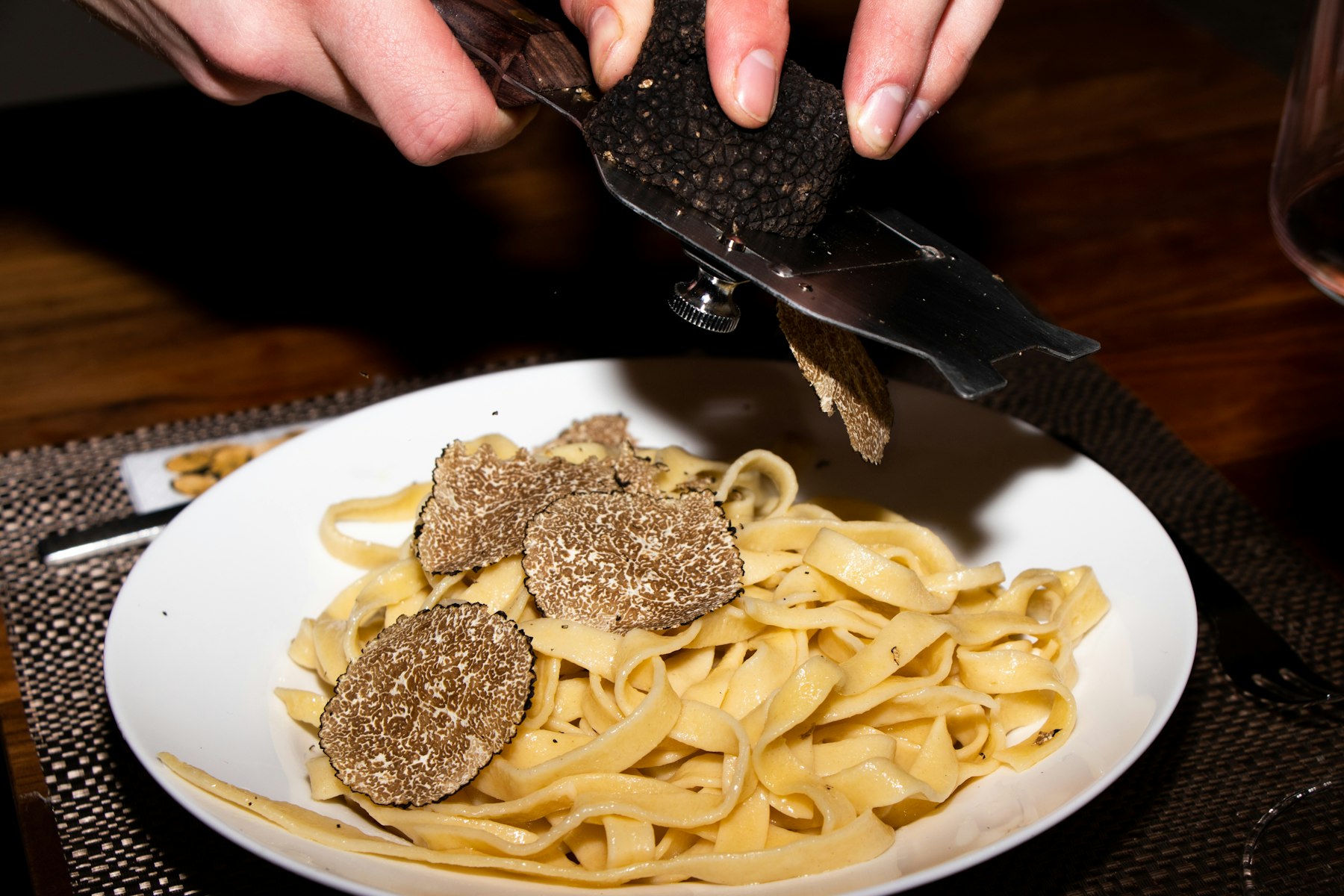 A truffle slicer shaving fresh white truffle over a plate of egg ribbon pasta