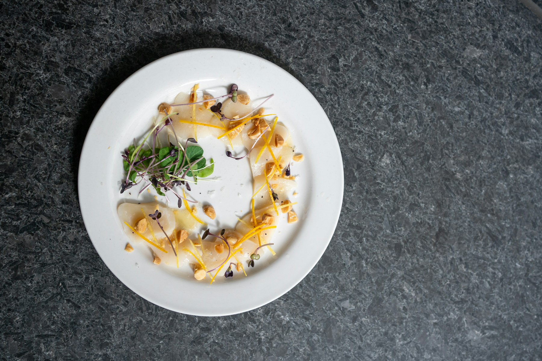 Filigraner Degustationsgang mit Zitrusfrüchten und Sprossen auf dunklem Steintisch