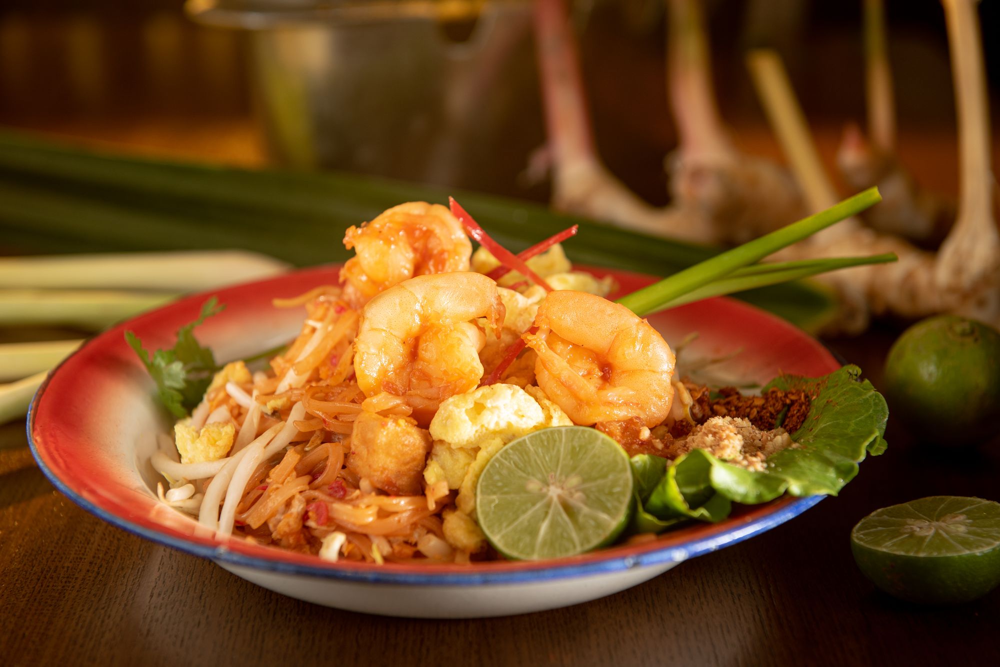 Pad Thai mit Garnelen, Limette, Sojasprossen und Frühlingszwiebel auf einem Emailteller