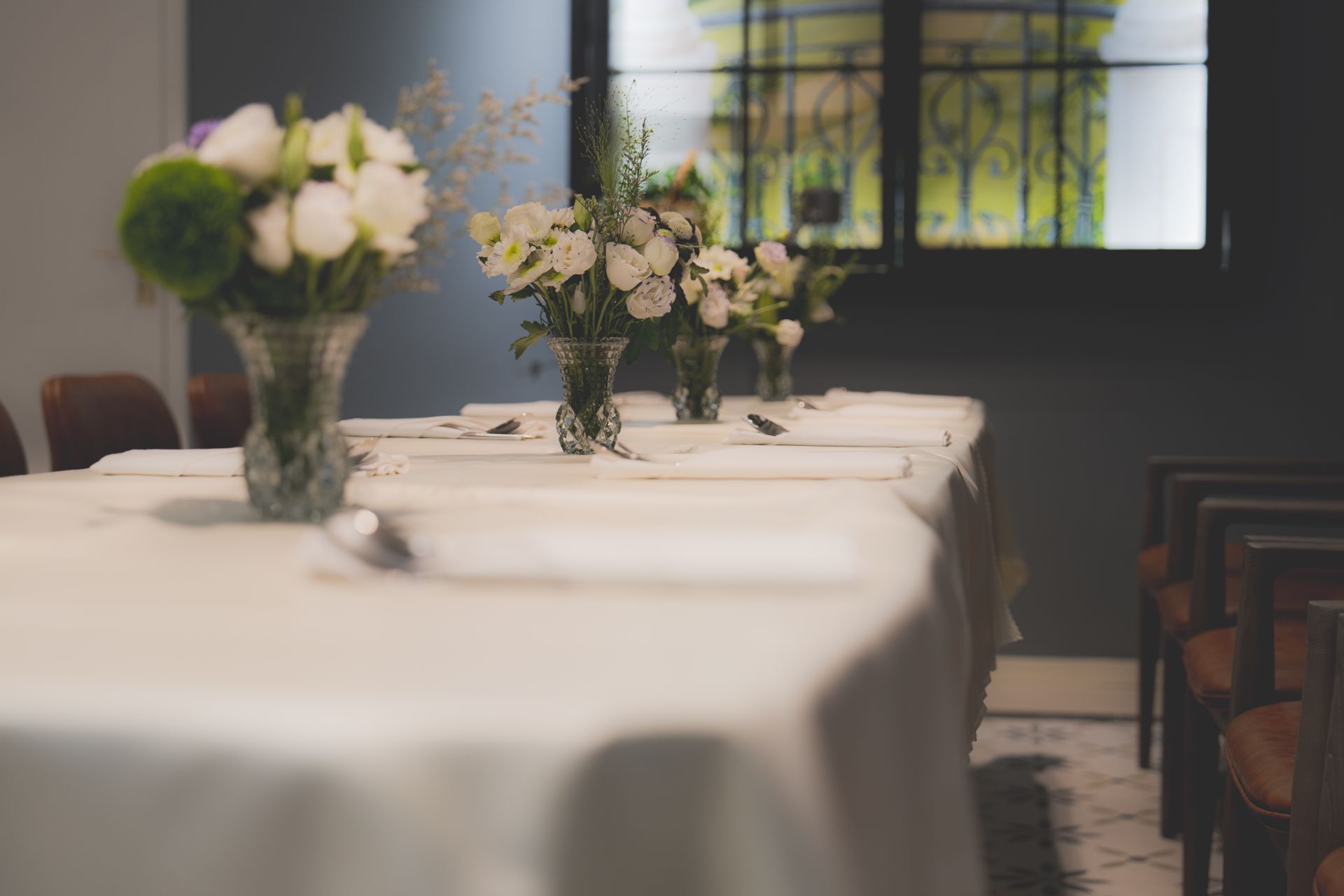 Row of tables laid with white linen and small flower vases before service