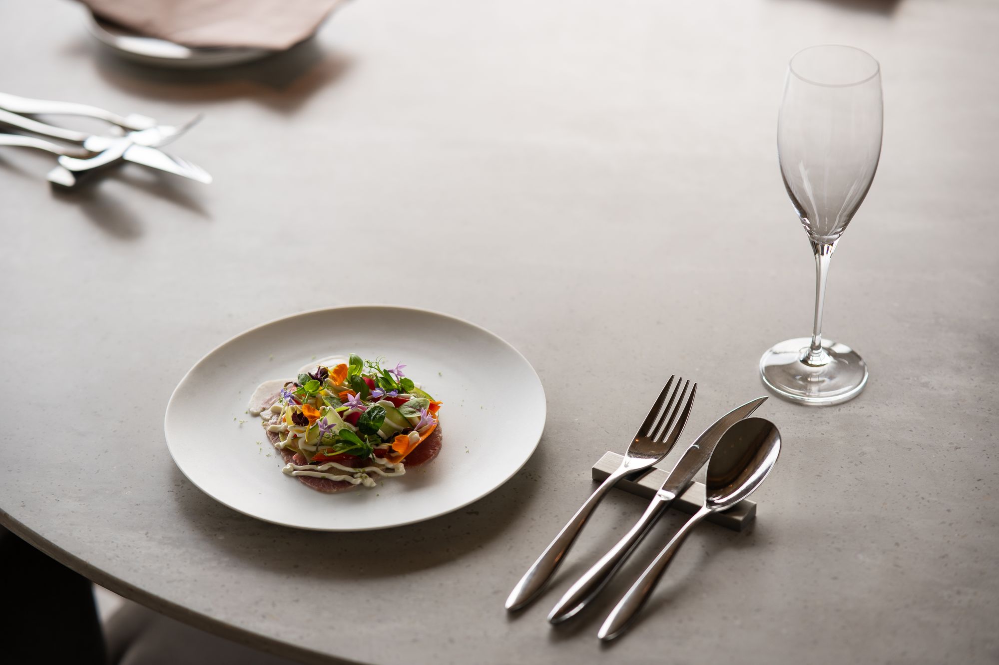 Single plated course, cutlery and an empty flute on a pale stone table