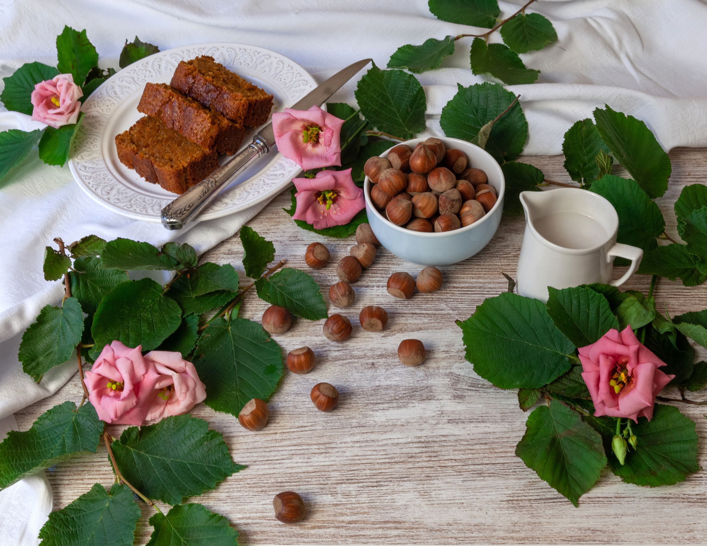 Slices of hazelnut cake on a white plate beside a bowl of whole hazelnuts