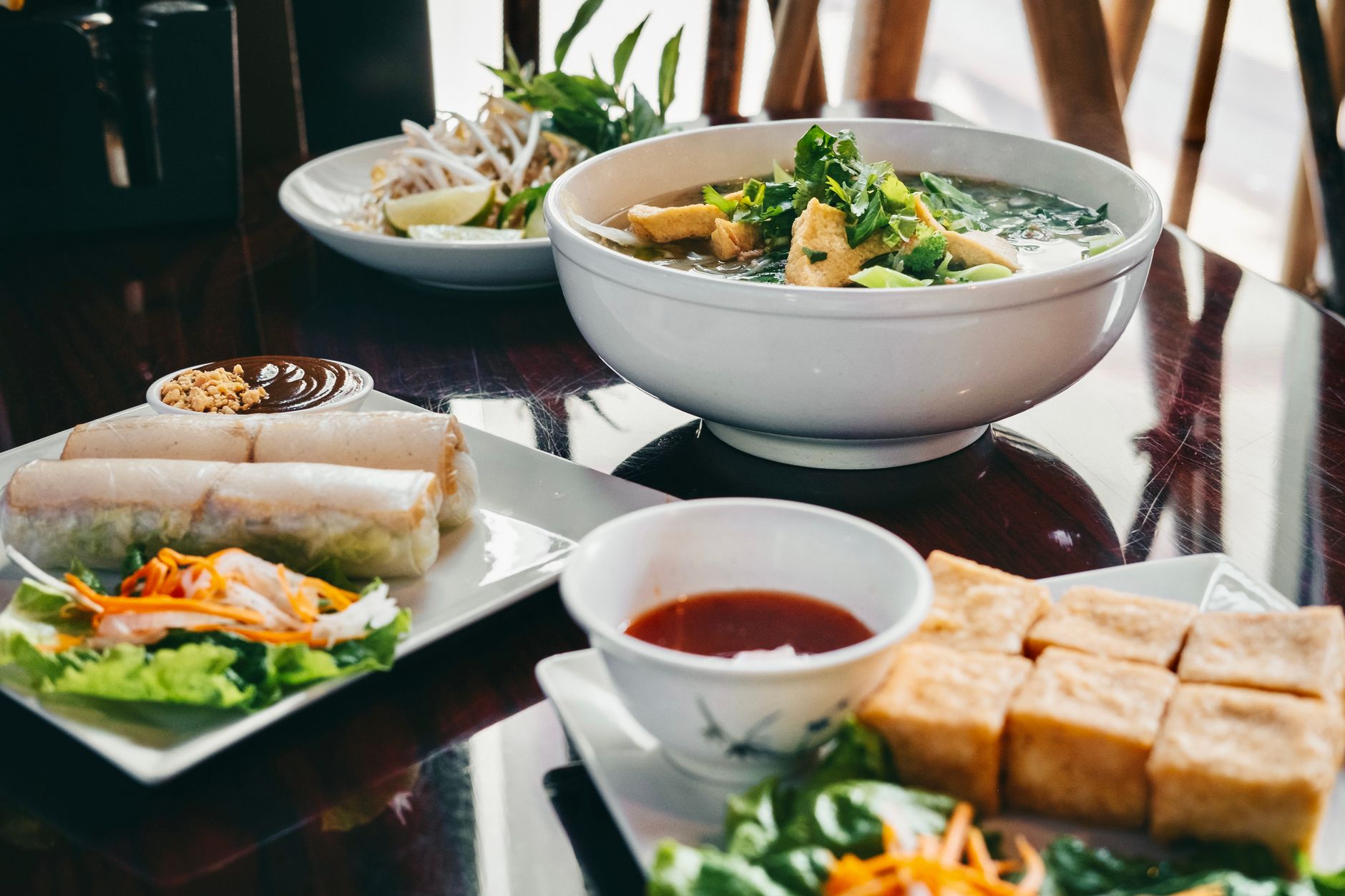 Cuencos de pho vietnamita, rollitos y tofu frito sobre una mesa de restaurante