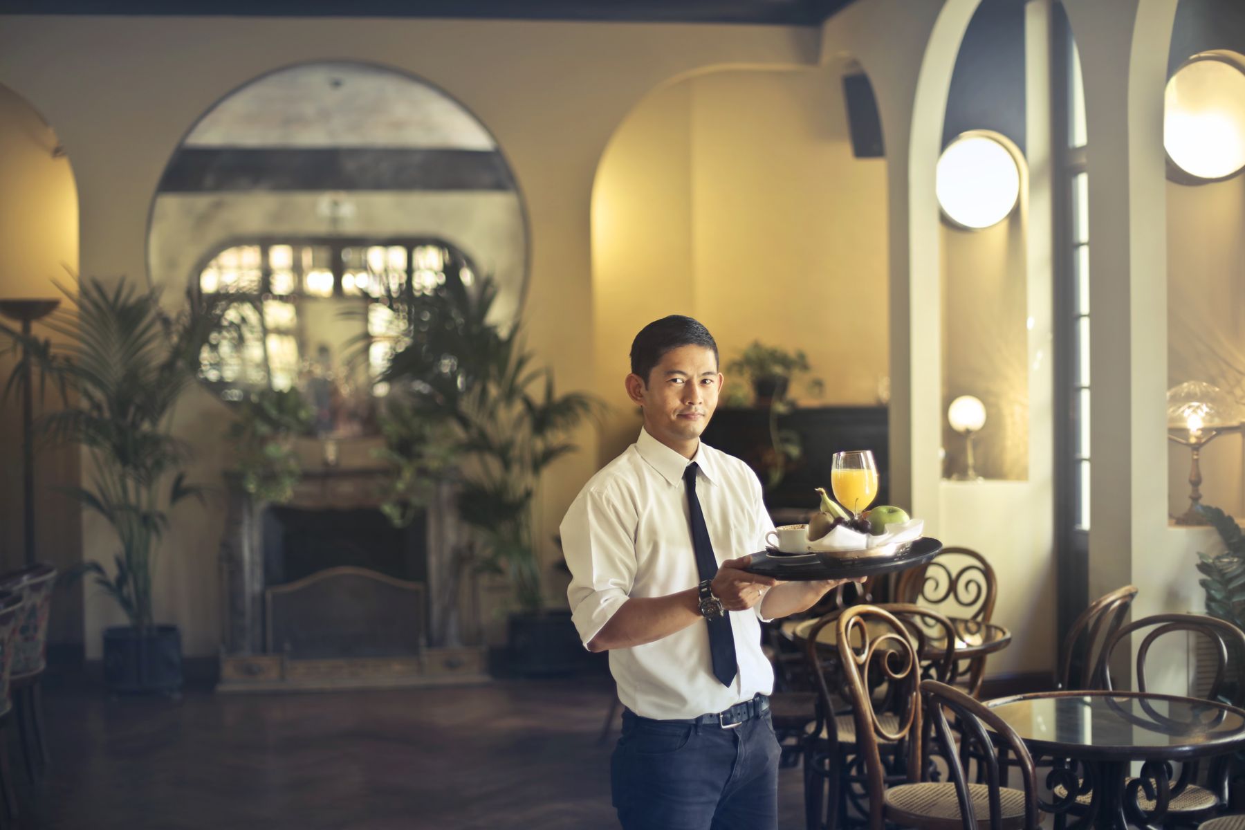 A waiter carrying a serving tray with drinks and fruit in an elegant restaurant