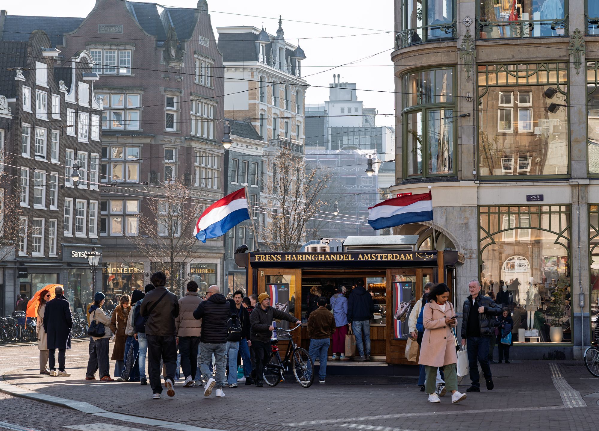 Queue at the Frens Haringhandel herring stand on Koningsplein in Amsterdam, beside Dutch flags