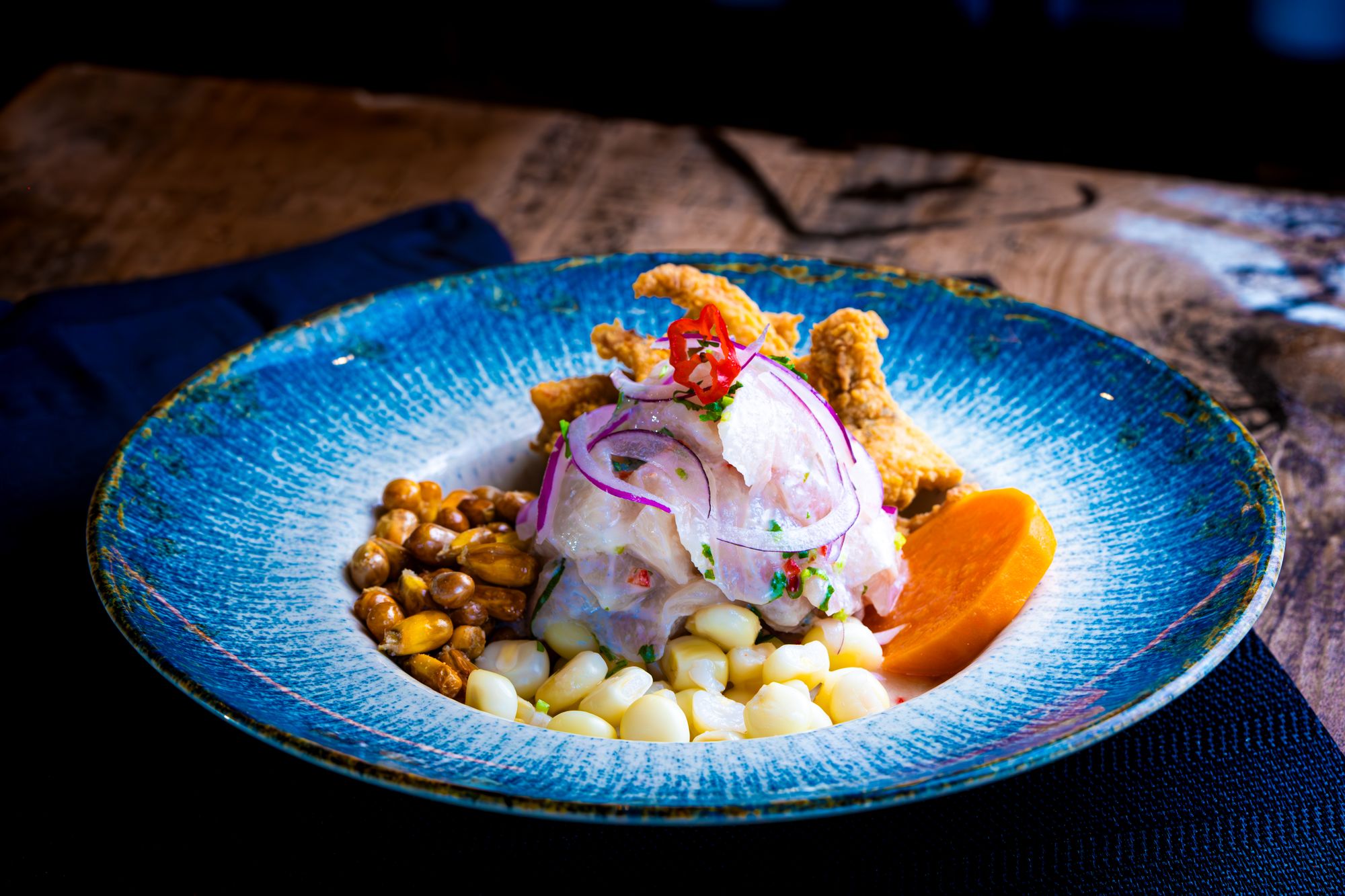 Peruvian cebiche with red onion, toasted corn, choclo and sweet potato in a blue bowl