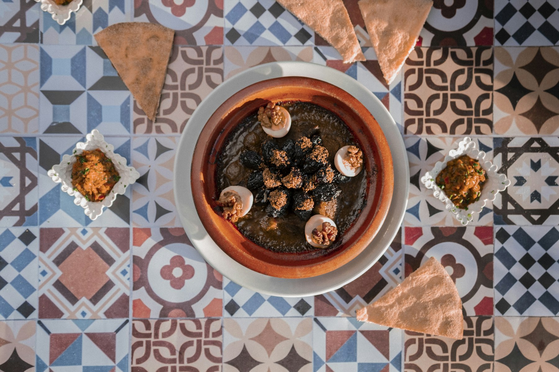 Tajín de cordero con ciruelas, nueces y huevo sobre una mesa marroquí de azulejos