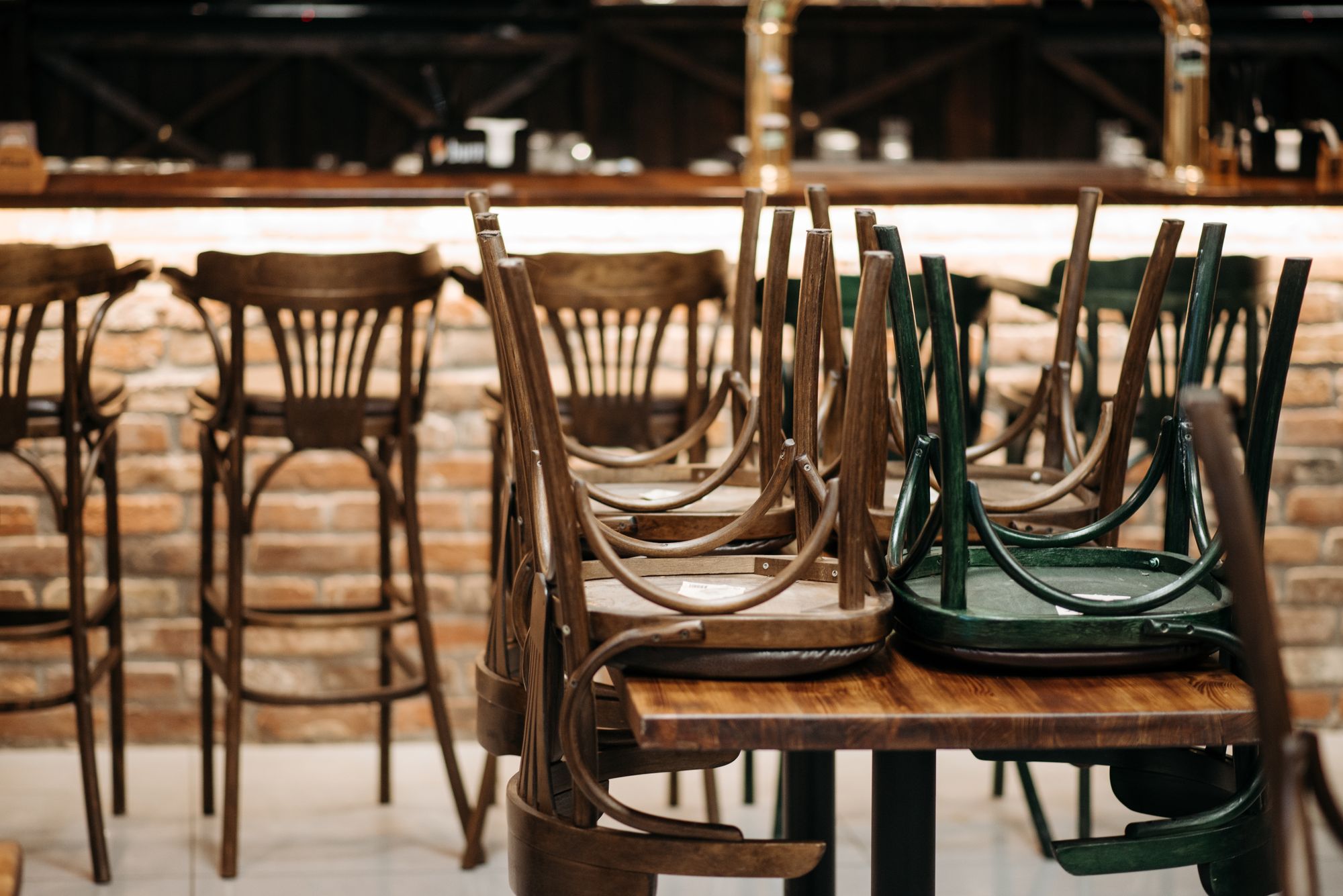 Wooden chairs stacked upside down on tables in front of an empty bar