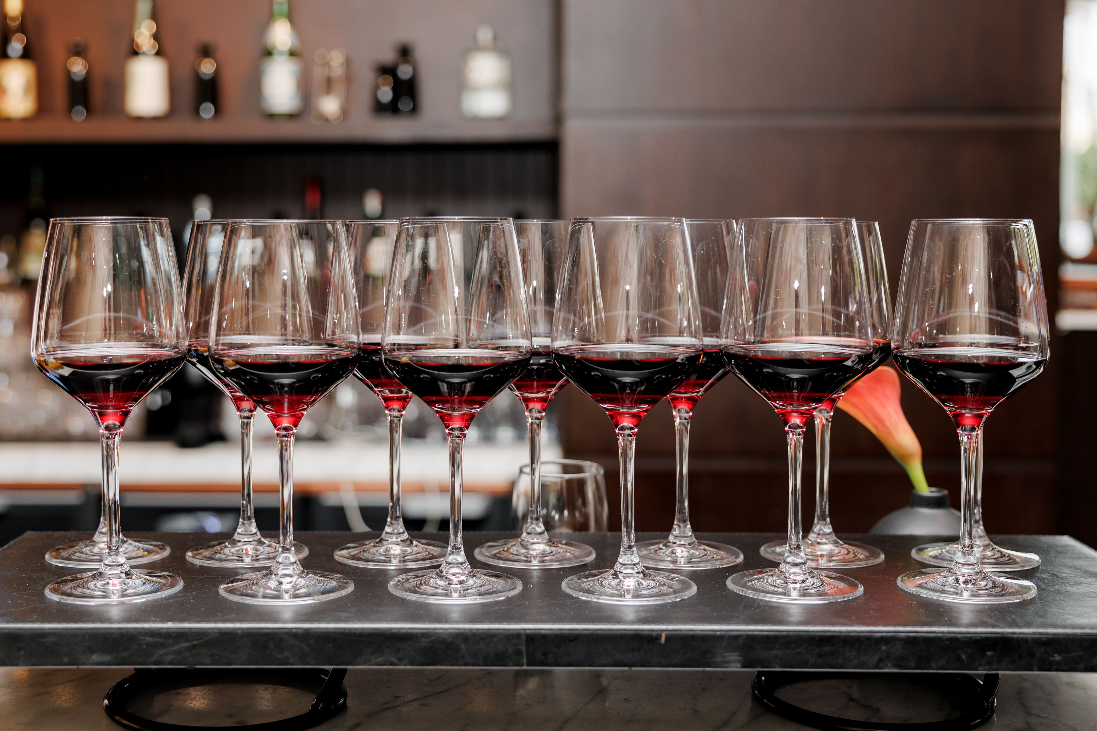 A row of stemmed glasses filled with red wine lined up on a restaurant bar