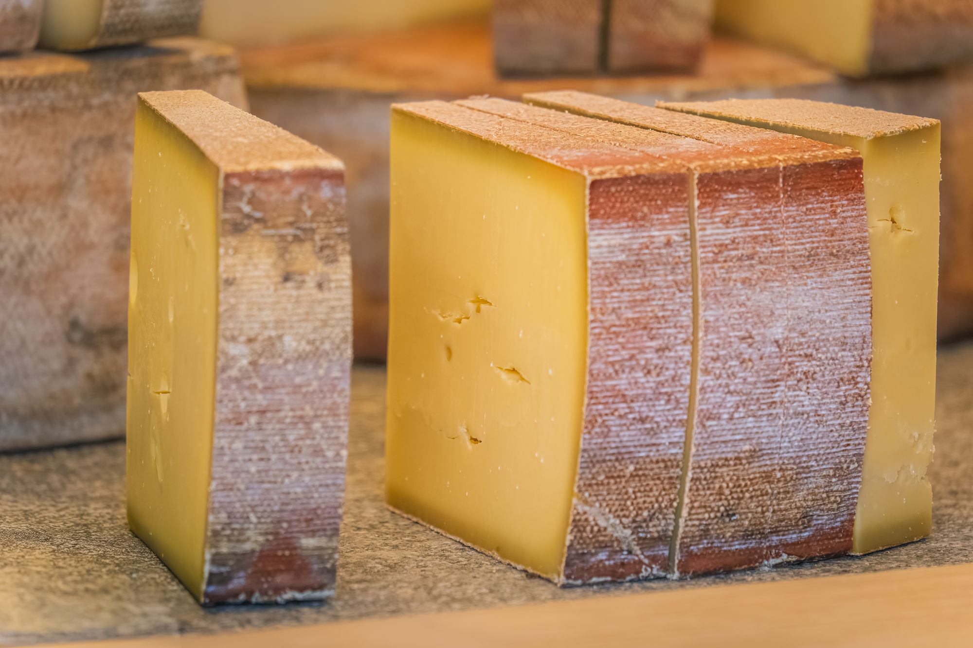 Cut blocks of hard mountain cheese with brushed rinds resting on a wooden counter