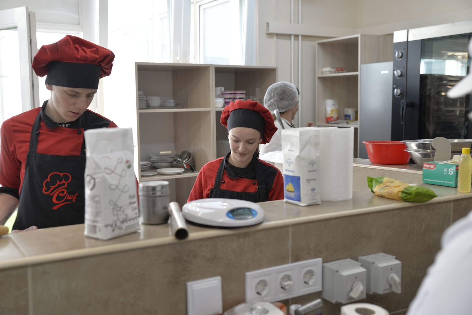 Due giovani chef in formazione con divisa rossa e cappello al lavoro in una cucina scuola