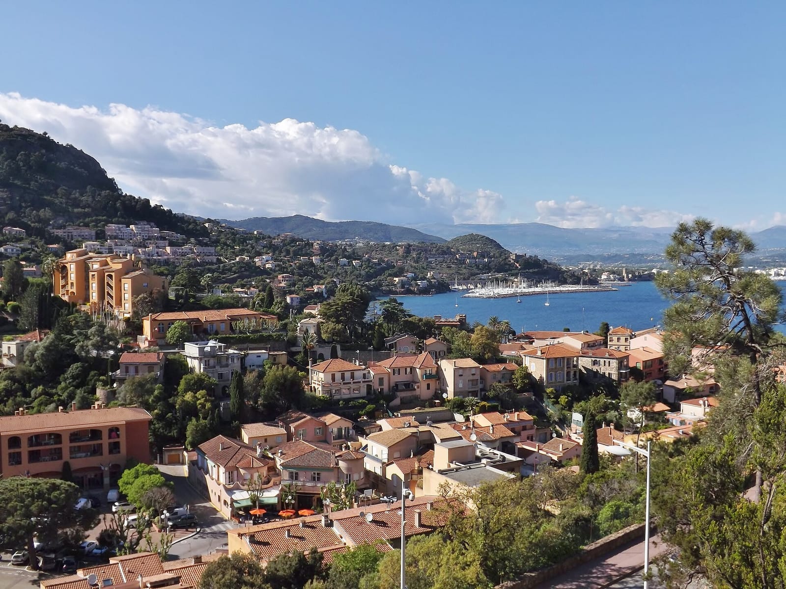 Terracotta roofs of Théoule-sur-Mer above a blue bay, with the Esterel hills and a marina behind
