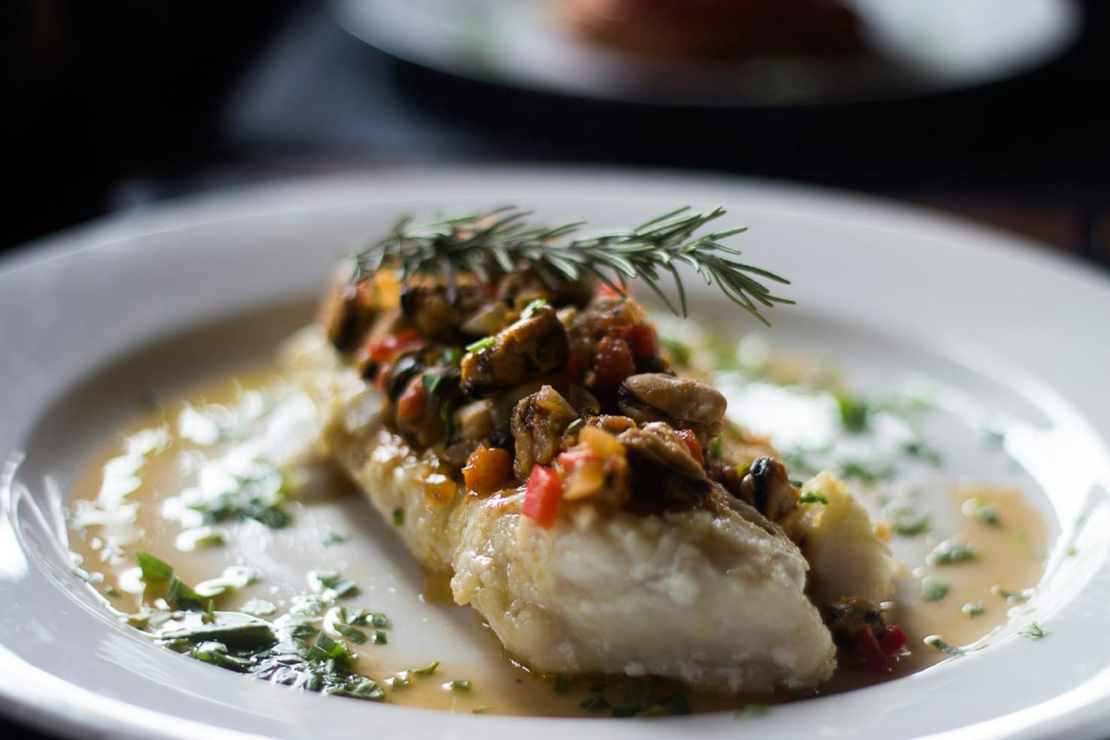 A fillet of white fish bathed in a golden olive oil sauce on a white plate