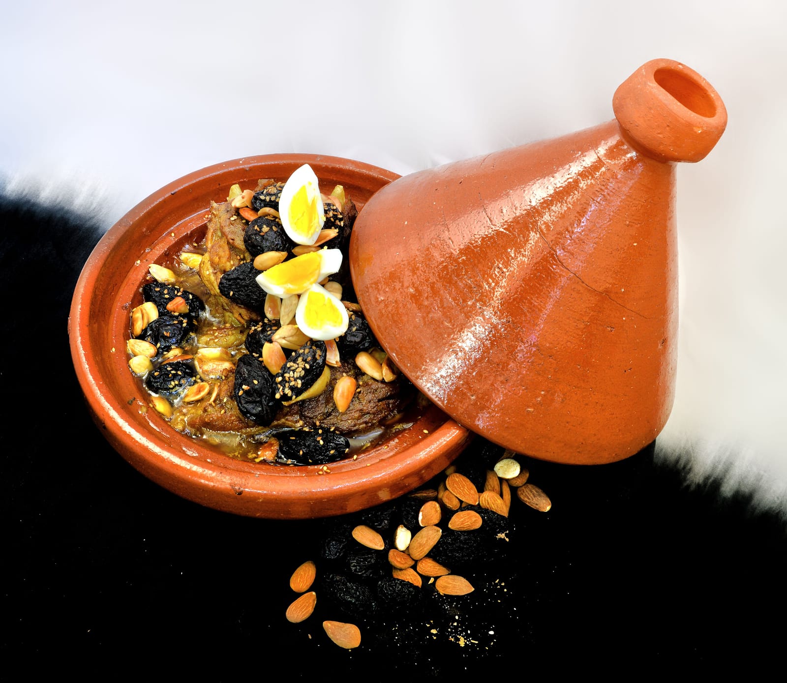 Un tajine d'inspiration marocaine aux amandes, pruneaux et œuf dur, avec le couvercle en terre cuite posé à côté