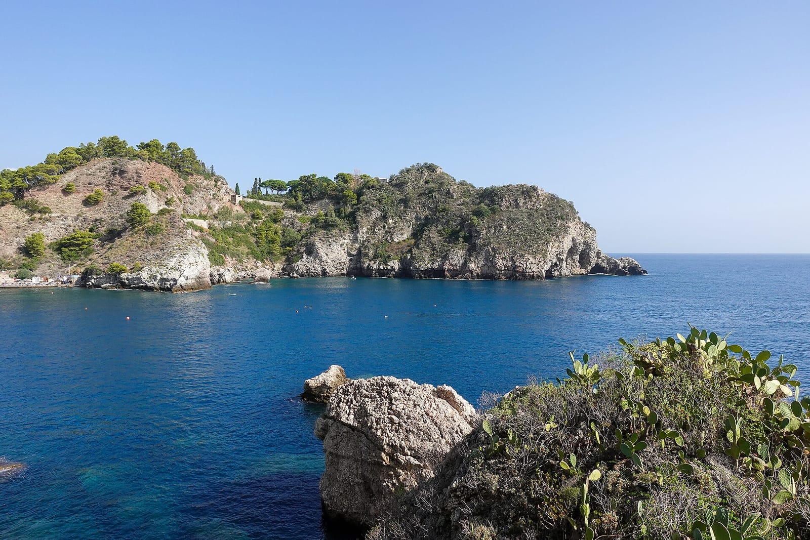 Rotsachtige kaap en diepblauwe Ionische Zee bij Isola Bella in Taormina, met vijgcactussen op de voorgrond