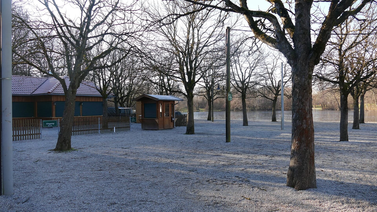 Closed beer garden kiosk and shuttered pavilion among bare trees in a Munich park in winter