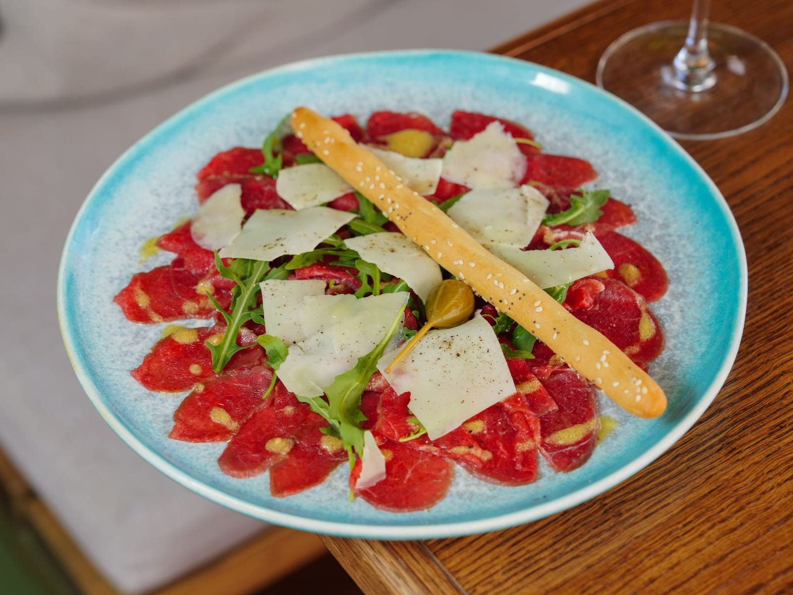 Carpaccio de bœuf avec copeaux de parmesan et un grissini sur une assiette bleue