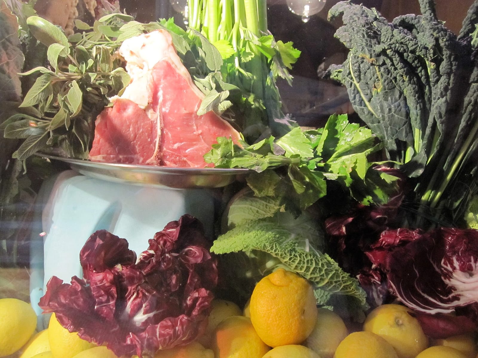 Raw bistecca alla fiorentina on a scale with cavolo nero, radicchio and lemons in a Florence trattoria window