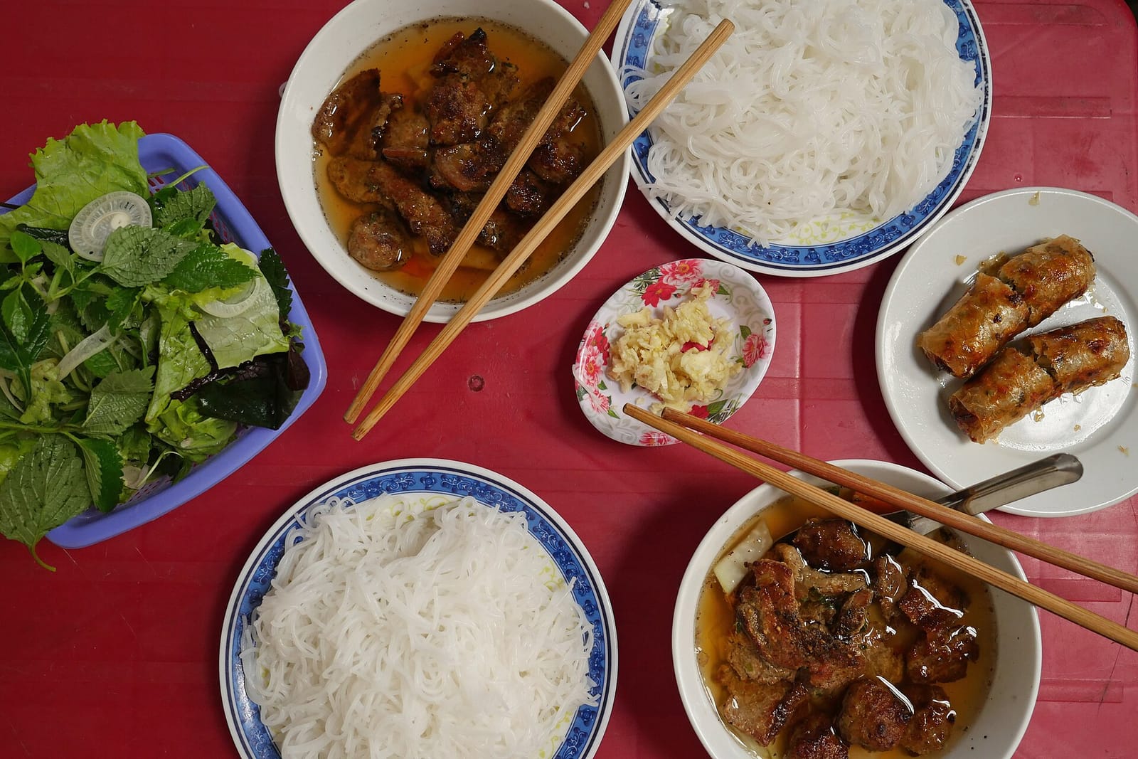 Bún chả au porc grillé, vermicelles, nems et herbes sur une table rouge