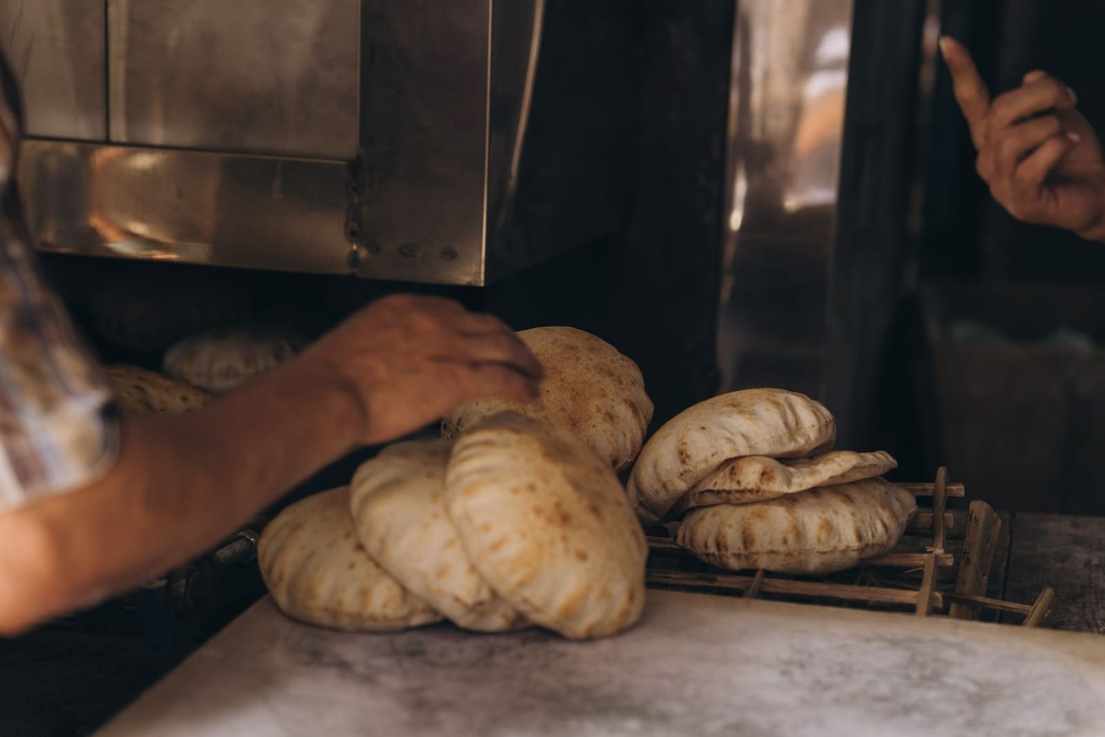 Hands pulling warm baladi flatbread from a stone oven at an Egyptian bakery