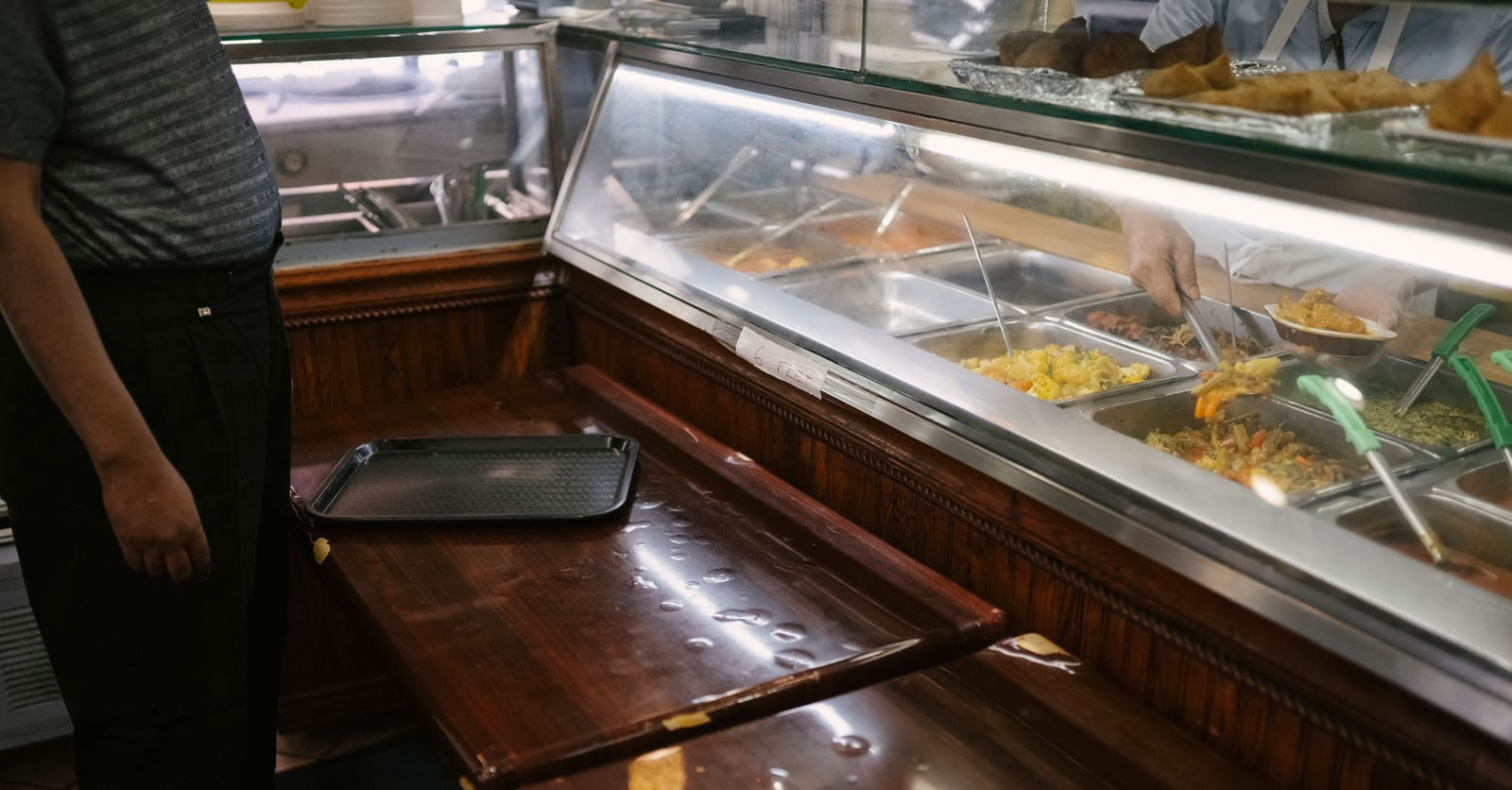 Un empleado sirve platos calientes en el mostrador de un comedor institucional