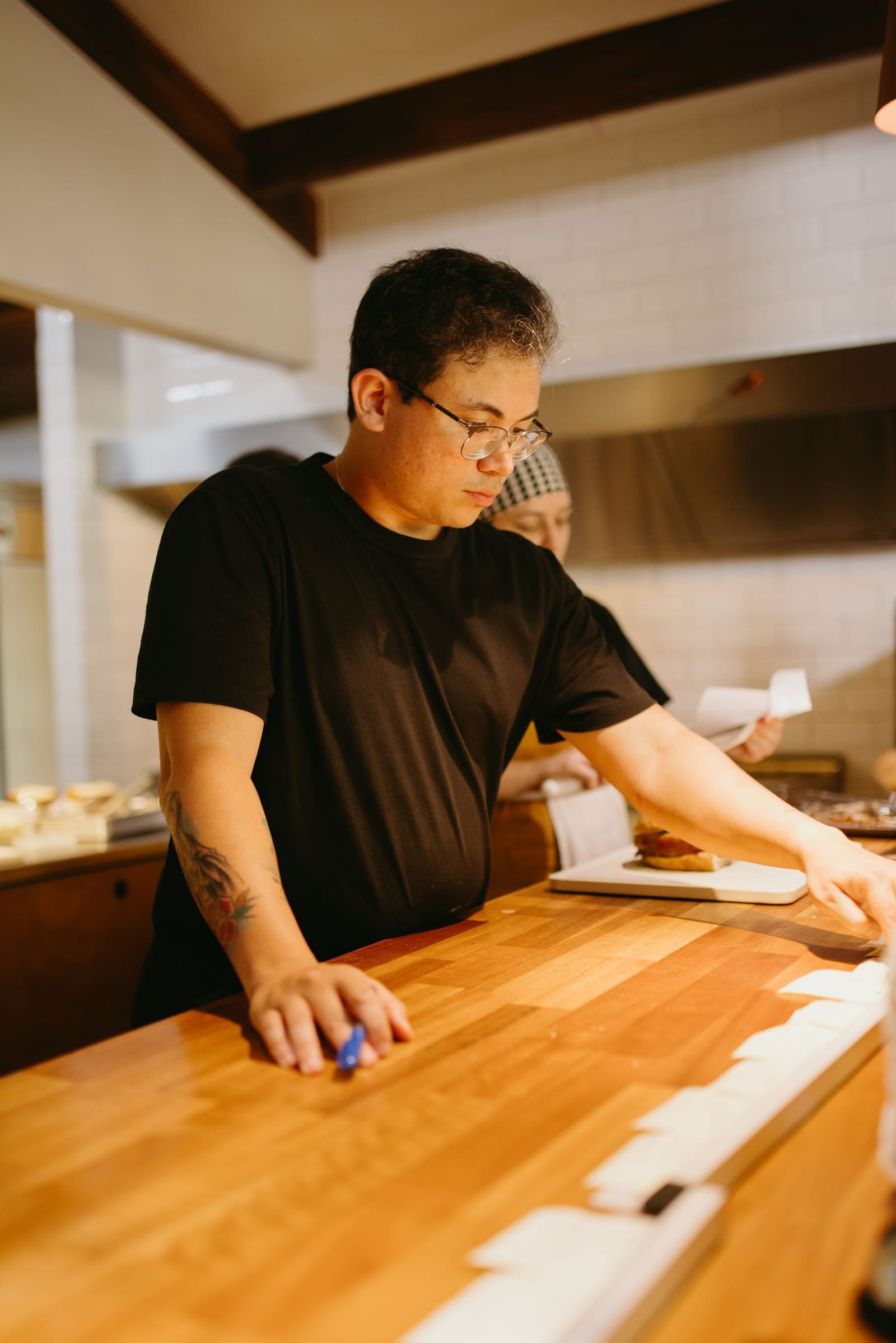 A chef plating a dish at a wooden open-kitchen counter