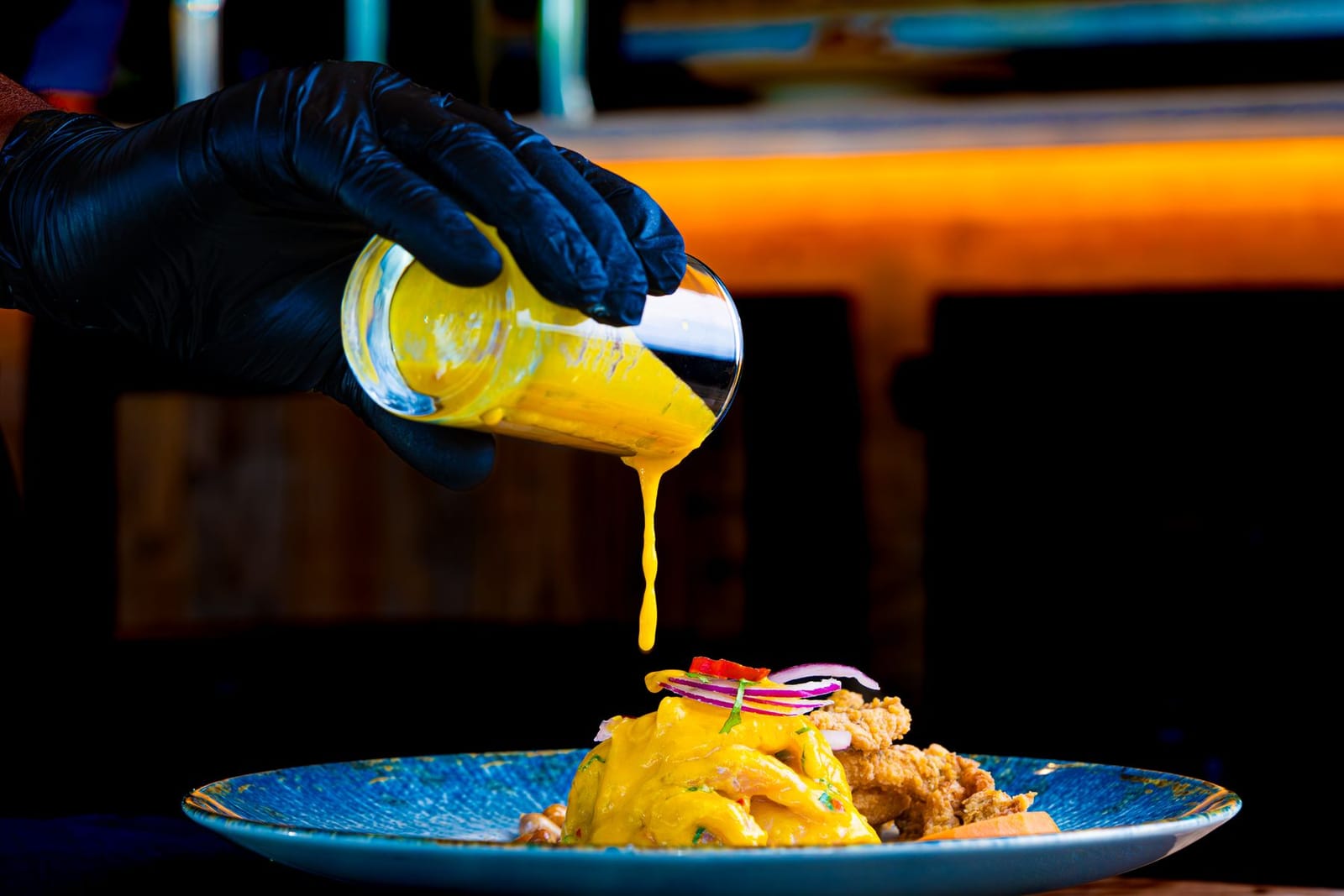 Chef in black gloves pouring sauce over a plated restaurant dish